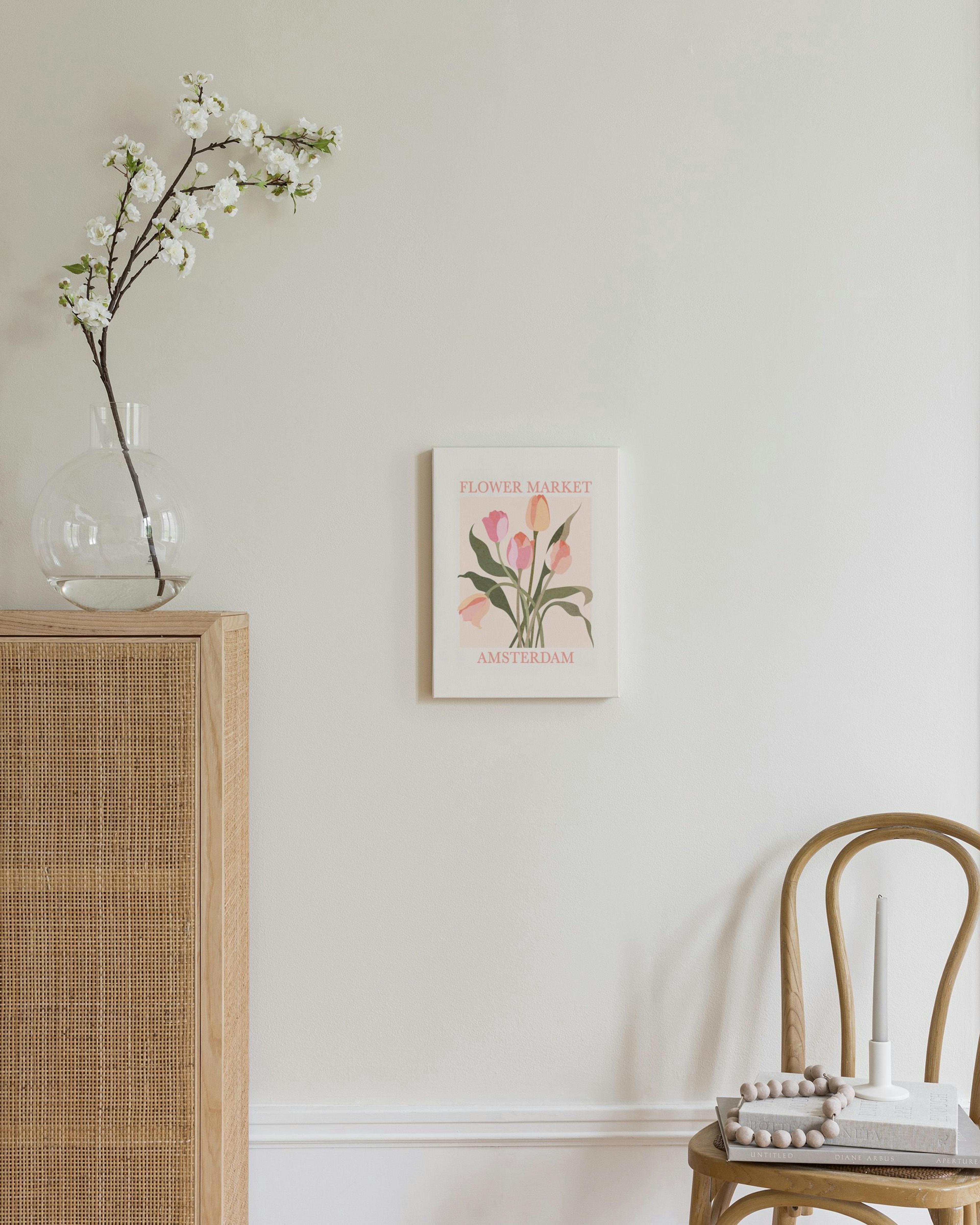 Toile Flower Market Amsterdam aux tulipes roses et orange, accrochée sur un mur blanc au-dessus dune chaise en bois.