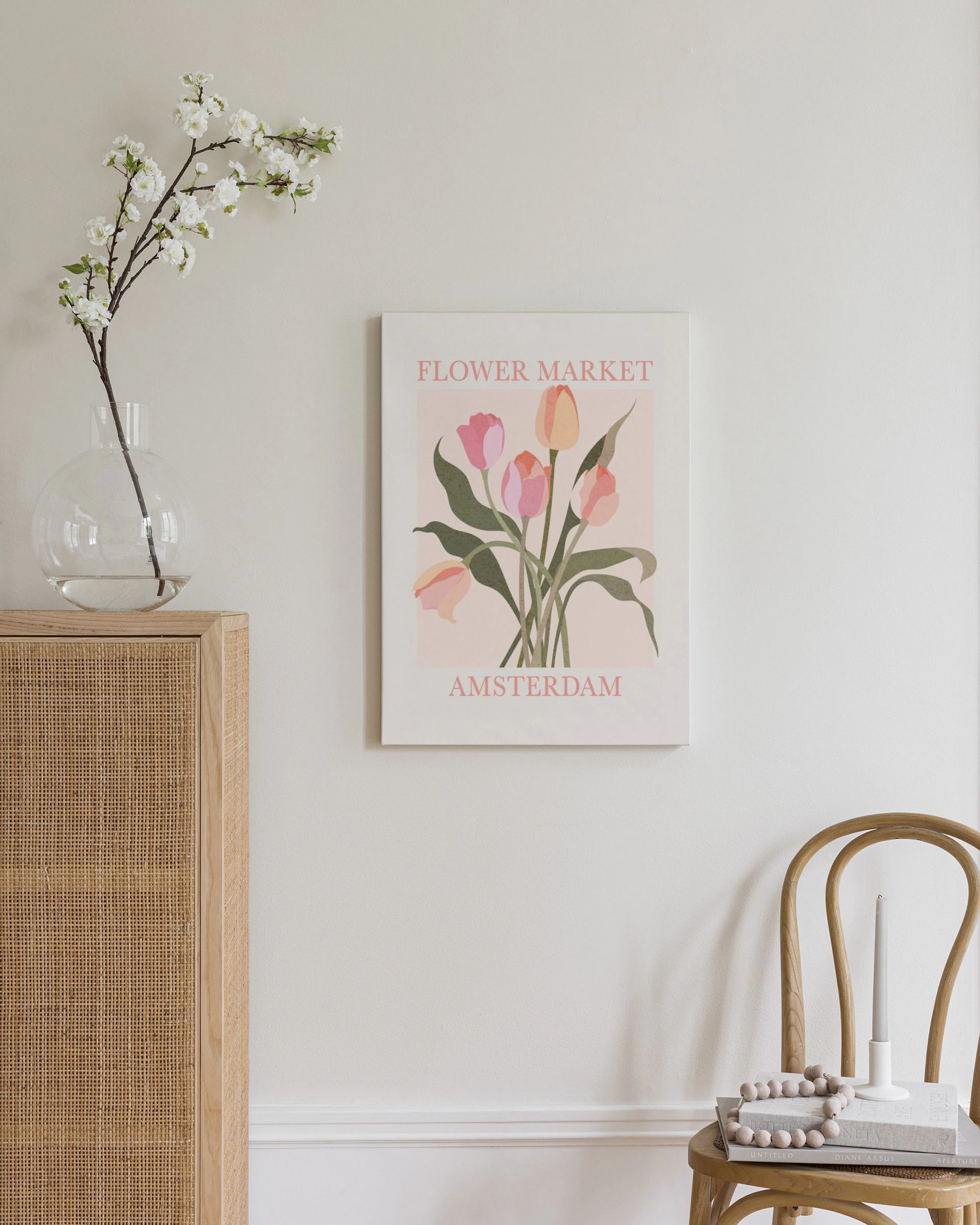 A canvas with a Flower Market Amsterdam print featuring pink and peach tulips, displayed on a light wall above a wooden chair.