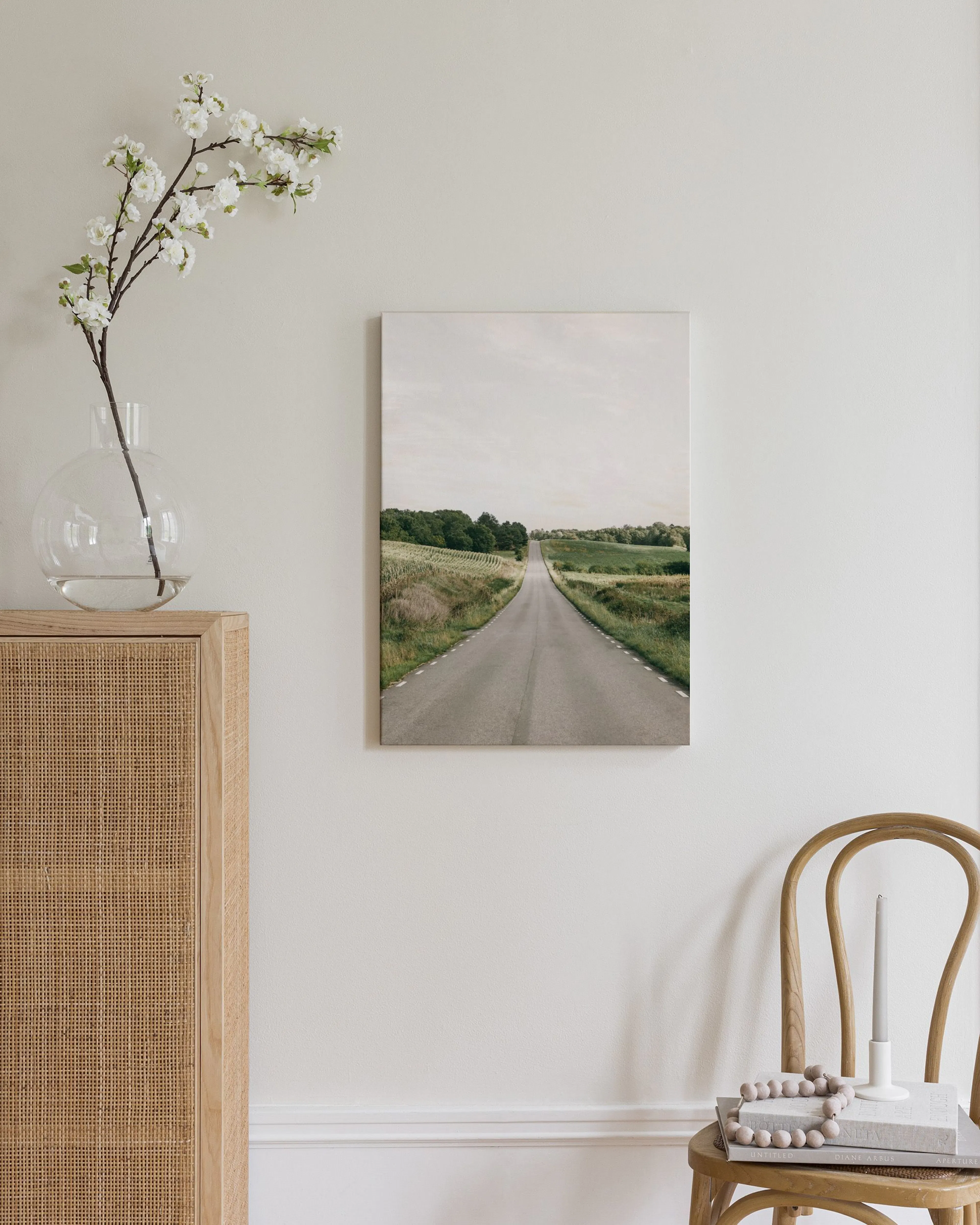 Leinwandbild mit einer Straße, die sich durch grüne Felder in der Ferne verliert, in einem hellen Wohnzimmer.
