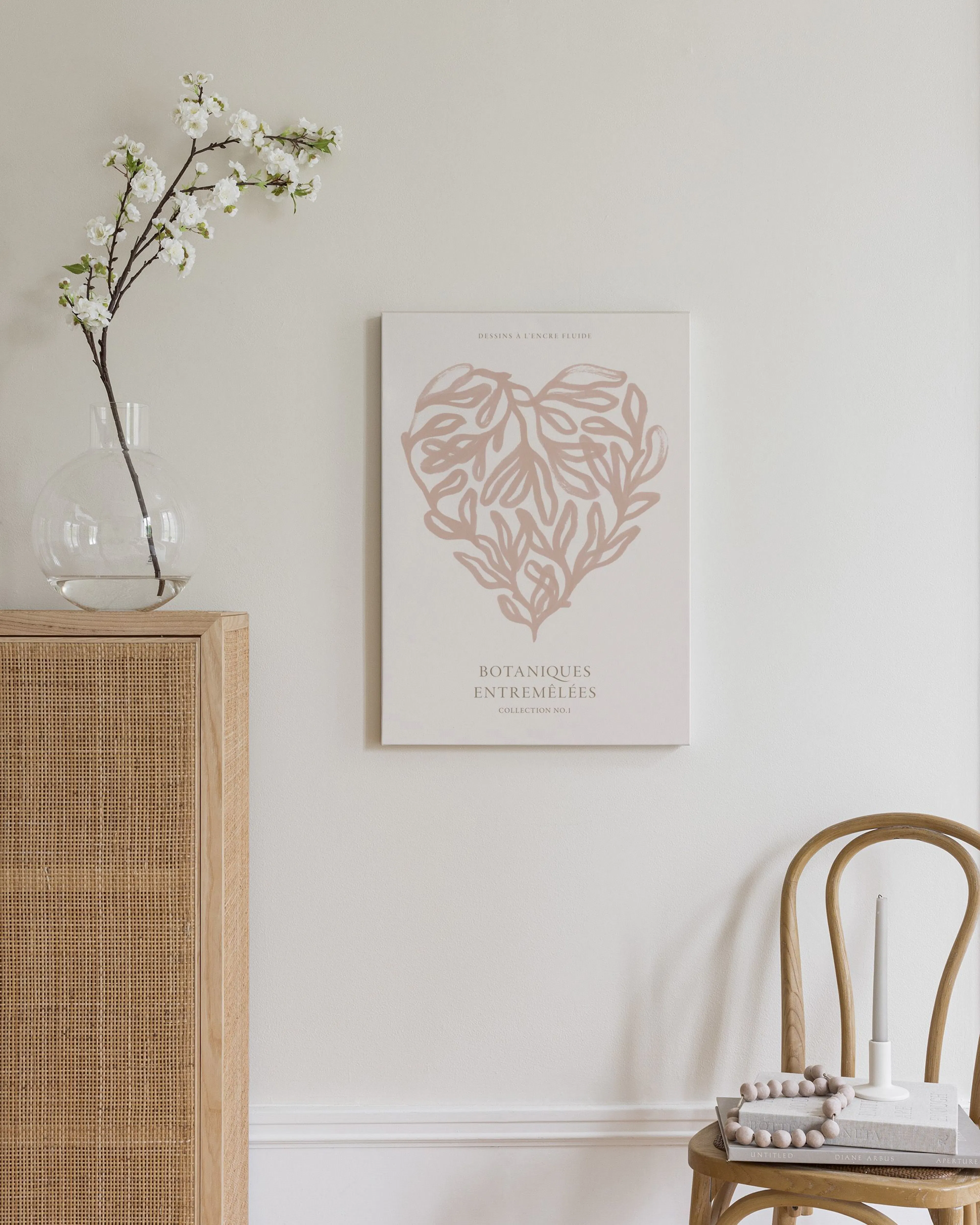 A canvas with a heart-shaped botanical design in soft pink on a light background, displayed in a bright room with a wooden cabin