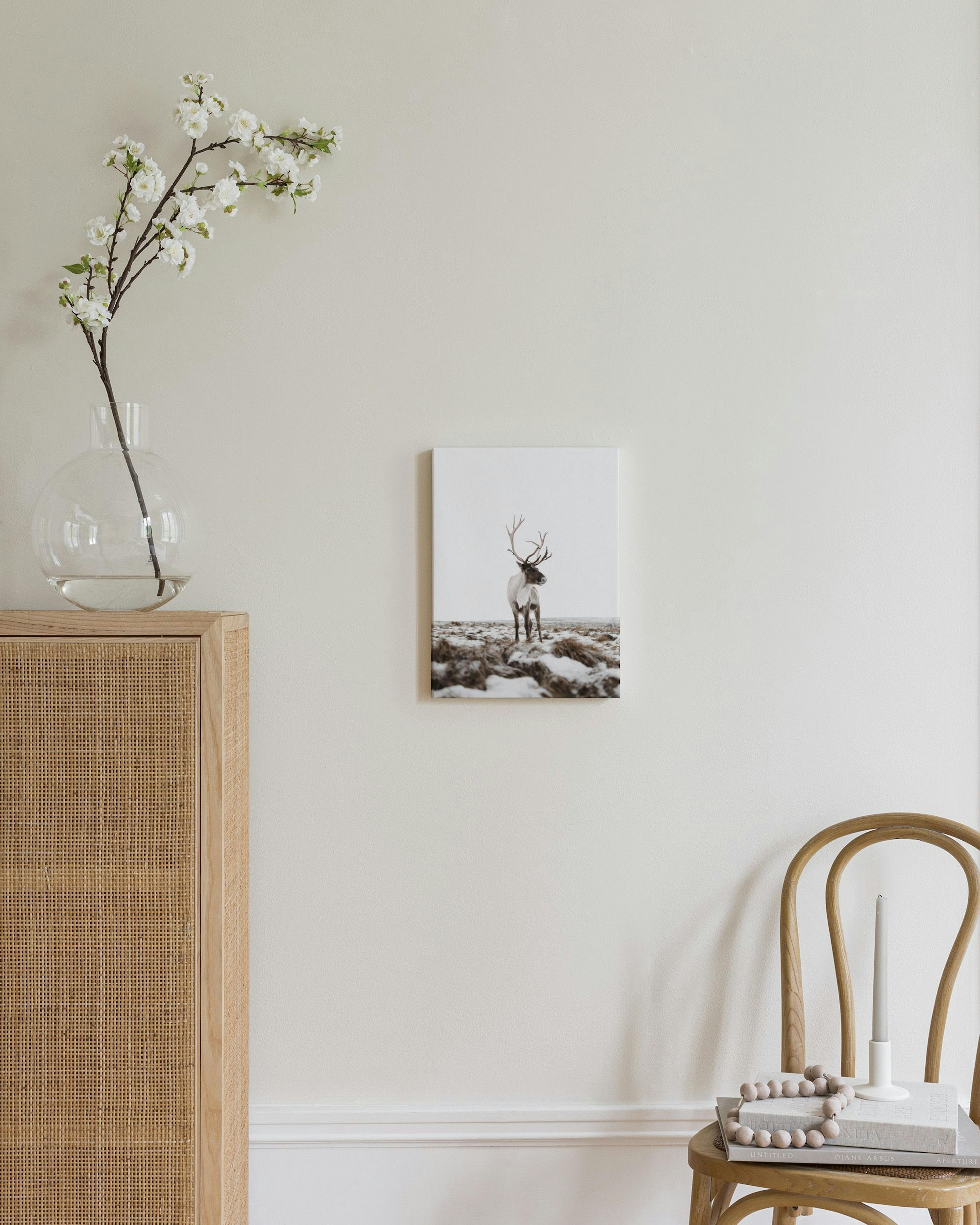 Toile dun caribou aux bois imposants sur un sol enneigé et herbeux, affichée au-dessus dune commode en rotin.