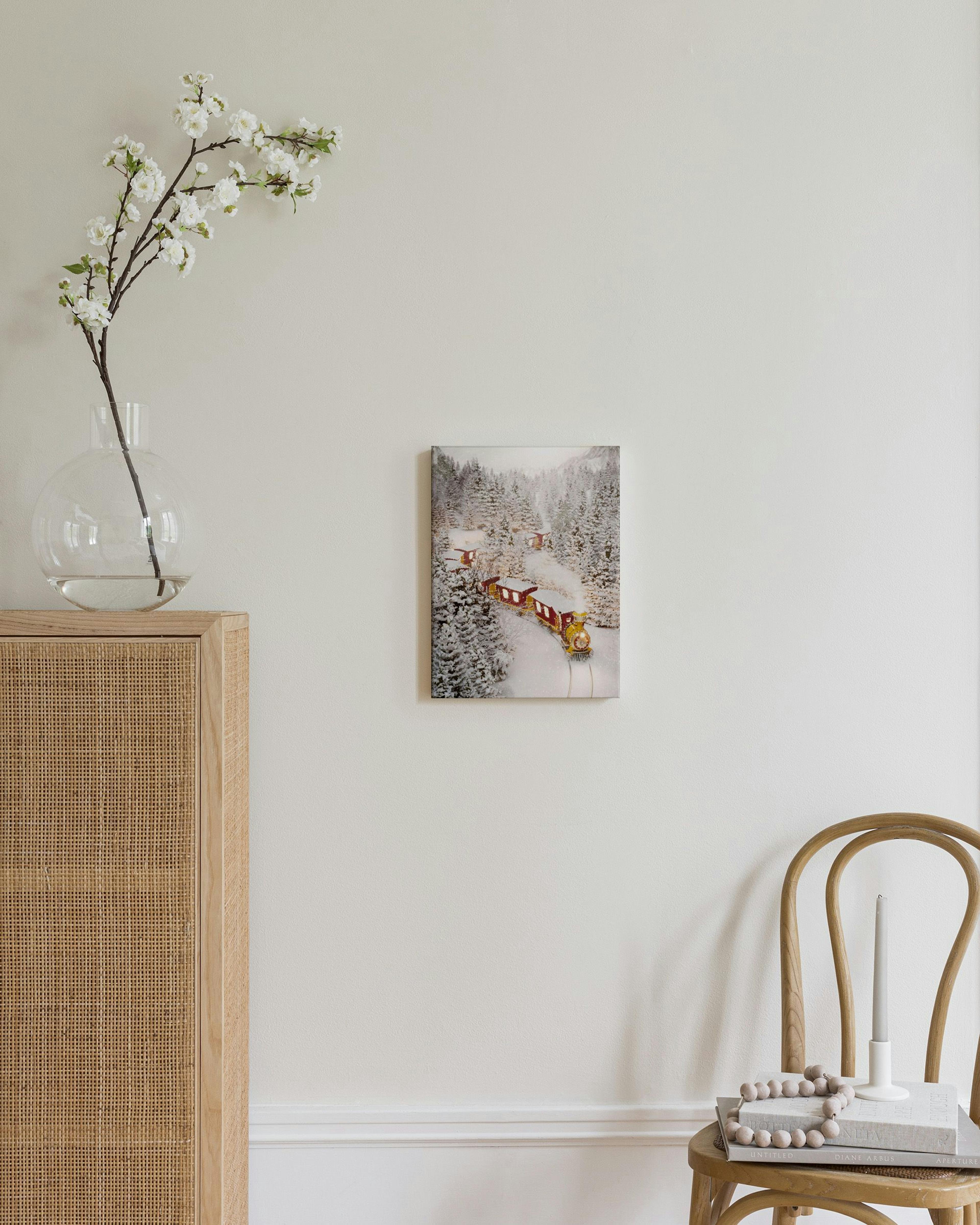 A canvas featuring a festive yellow and red train traveling through a snow-covered forest, displayed above a wooden nightstand i