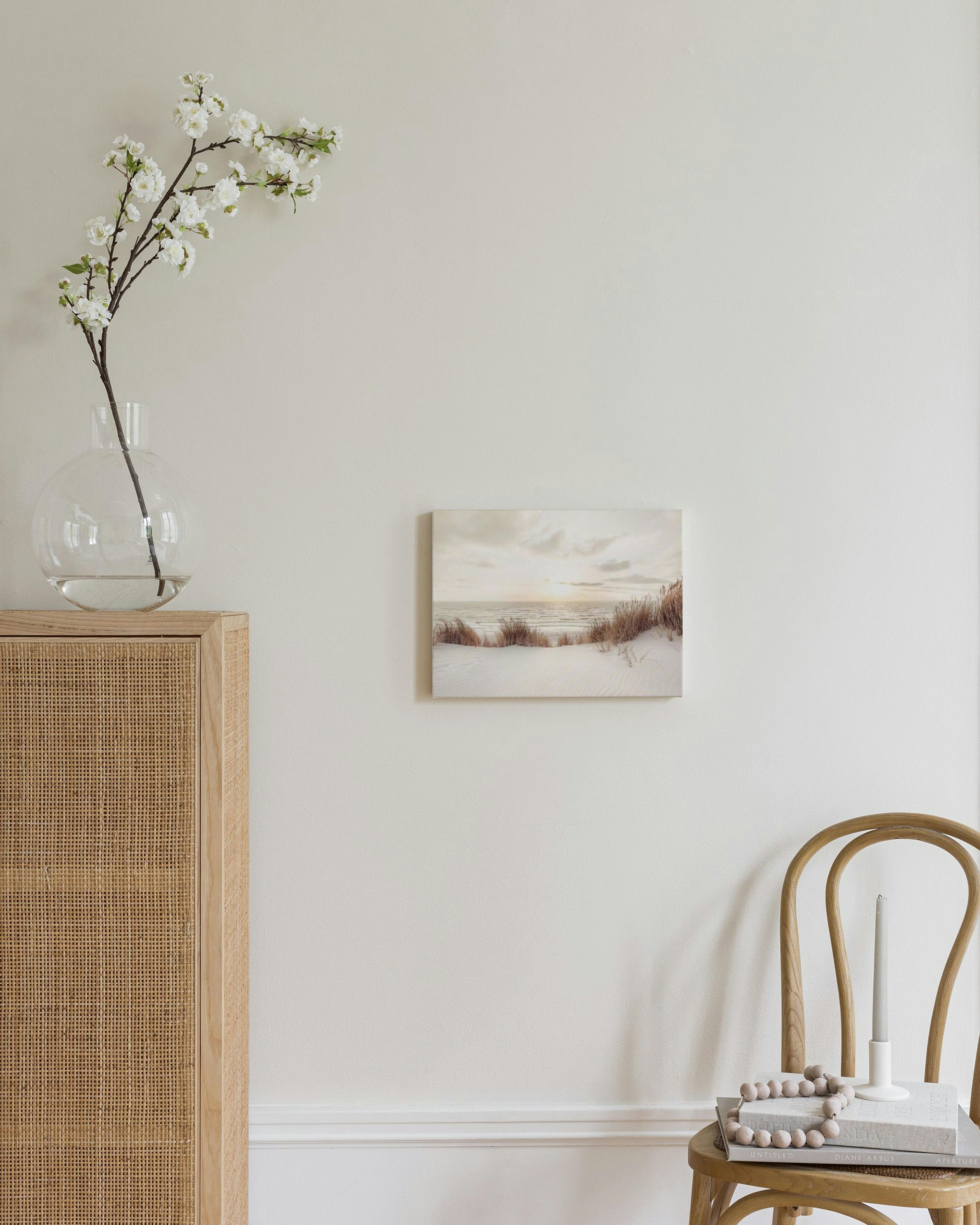 Leinwandbild einer Dünenlandschaft am Meer bei Sonnenuntergang, über einem Rattan-Sideboard im Schlafzimmer.