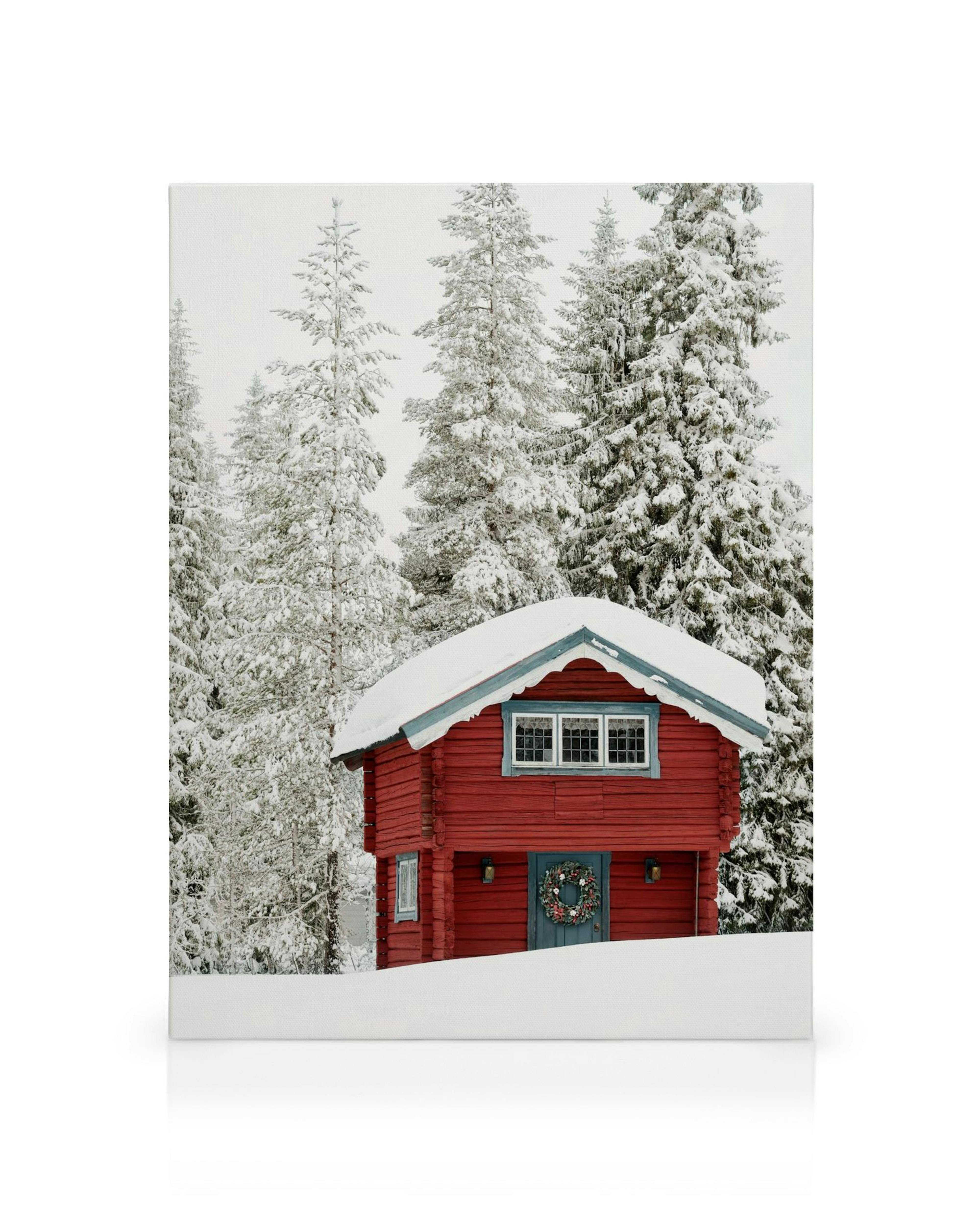 Kanvaasi punaisesta mökistä lumisessa maisemassa. Mökin edessä on sininen ovi ja joulukranssi.