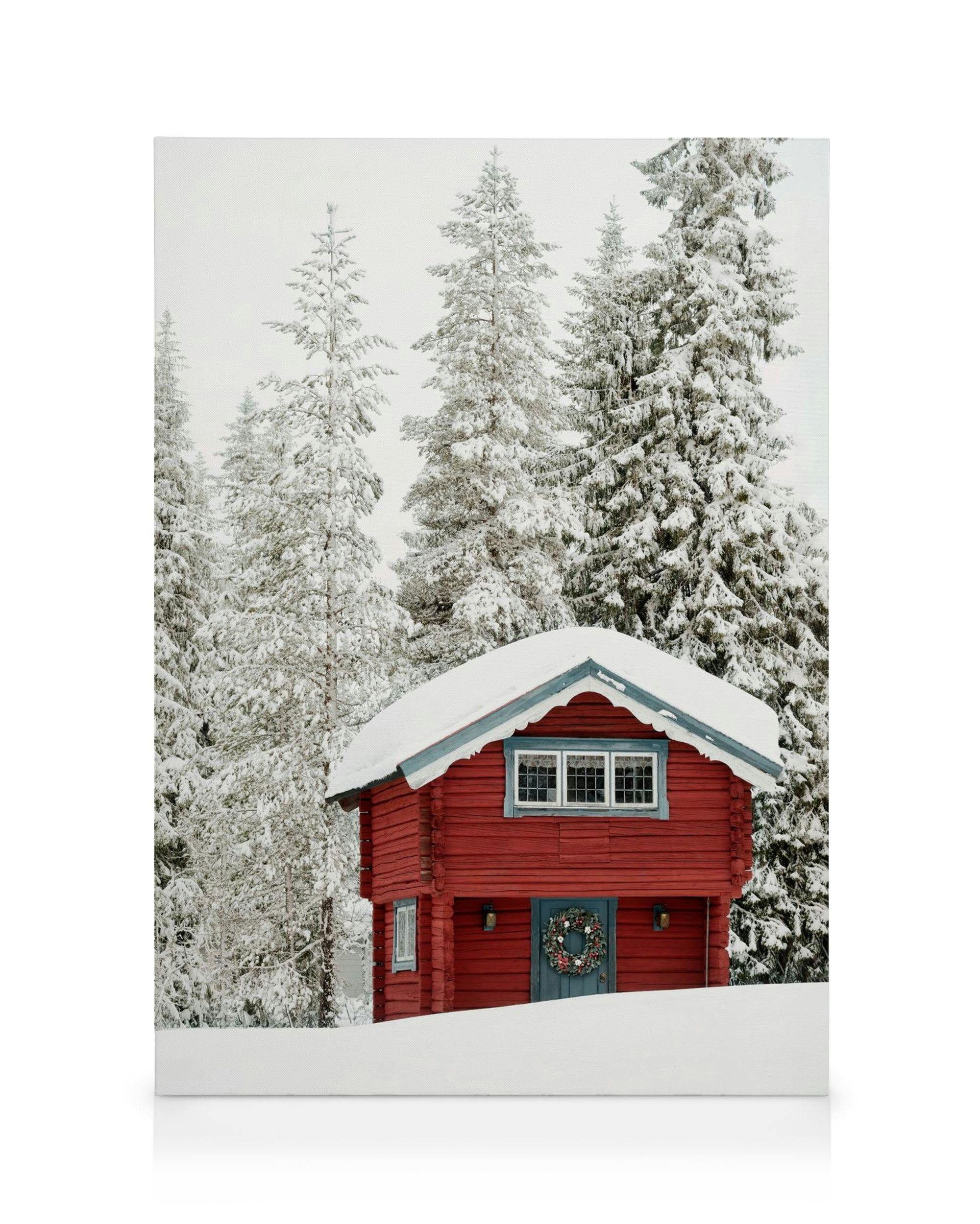A canvas showing a red wooden cabin with a wreath on the door, surrounded by snow-covered pine trees and a white landscape.