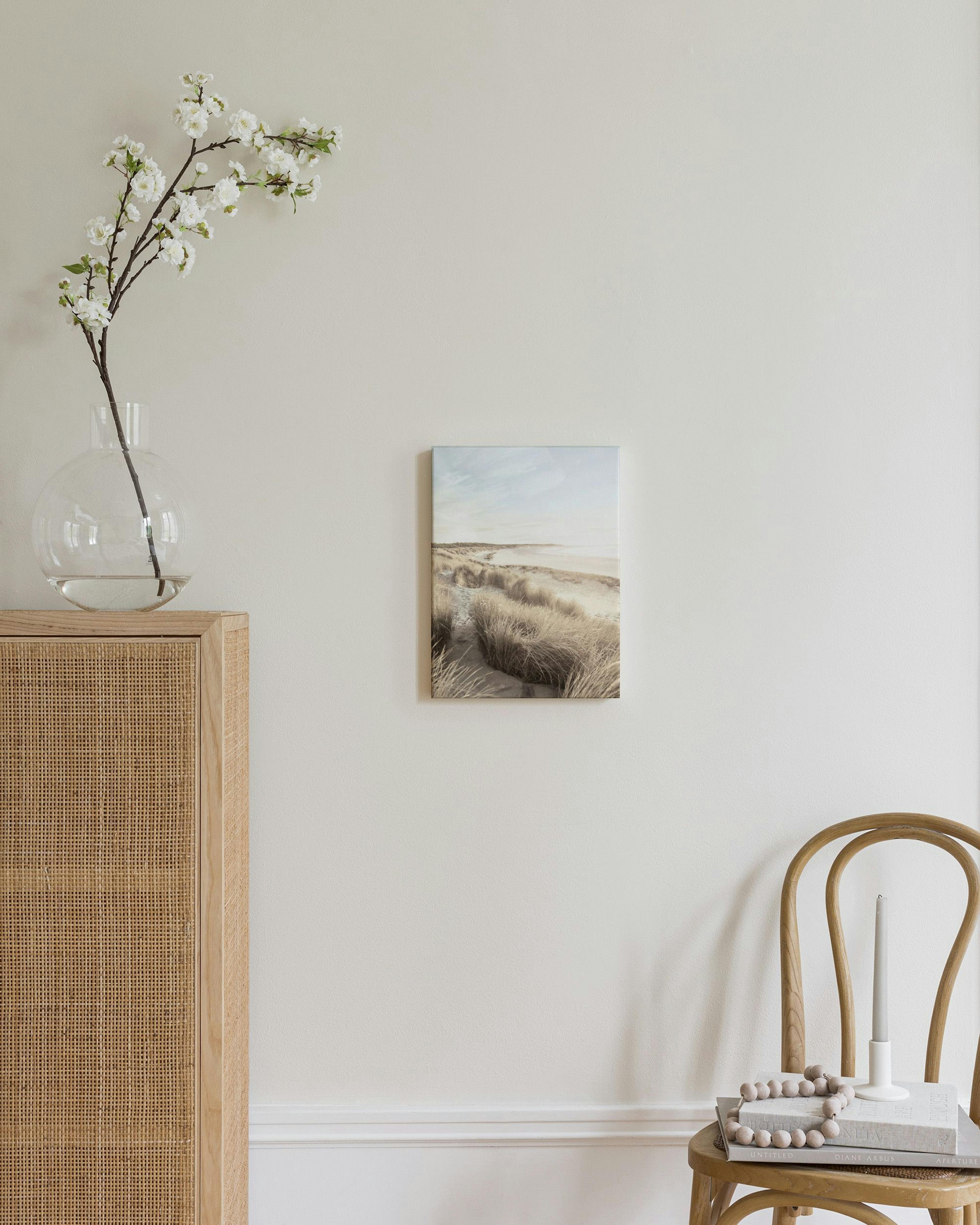 Lienzo de dunas de playa con hierba seca bajo un cielo nublado, colgado sobre una cómoda de madera en un dormitorio.
