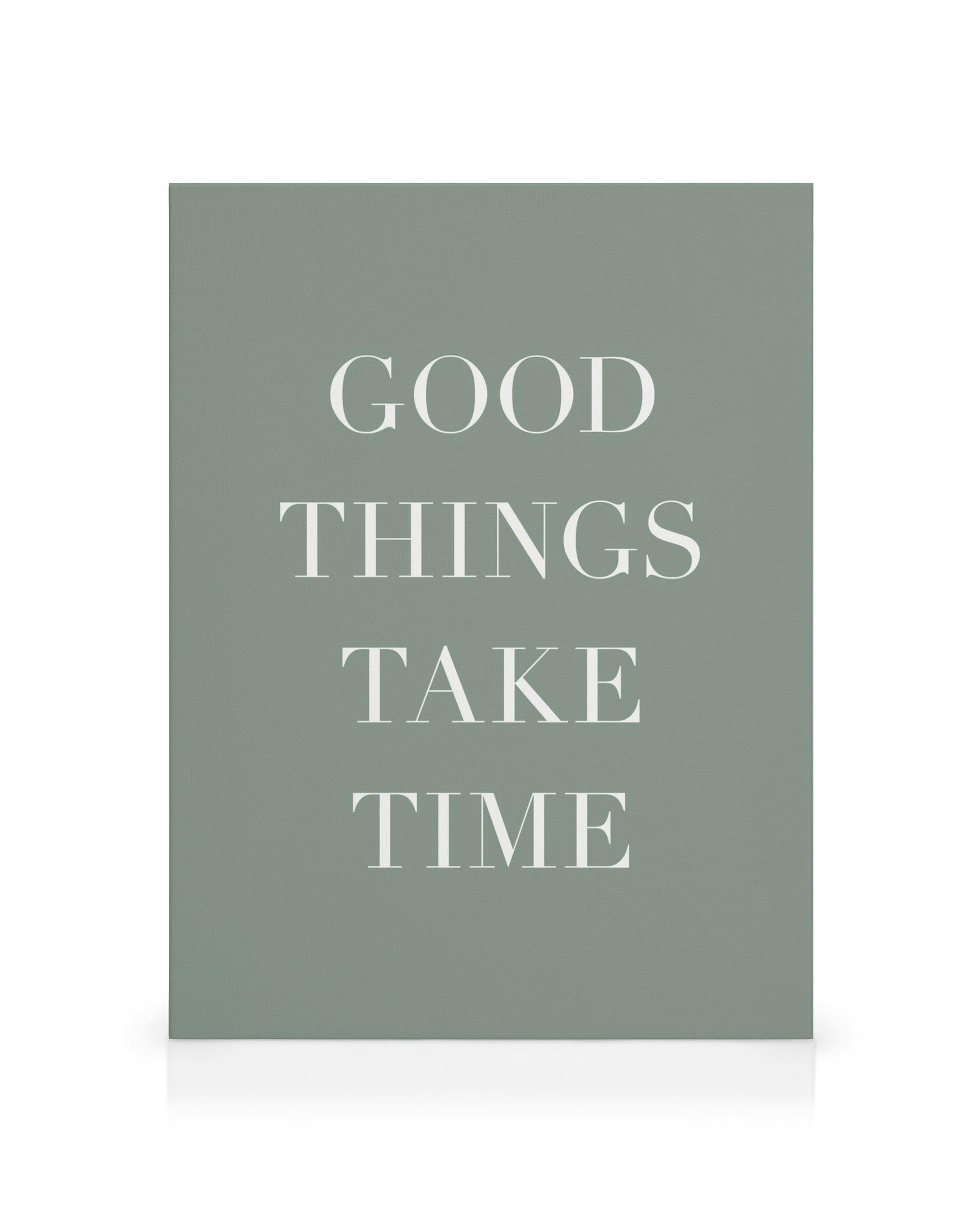 Et lærred med teksten GOOD THINGS TAKE TIME i hvid skrift på en grågrøn baggrund.