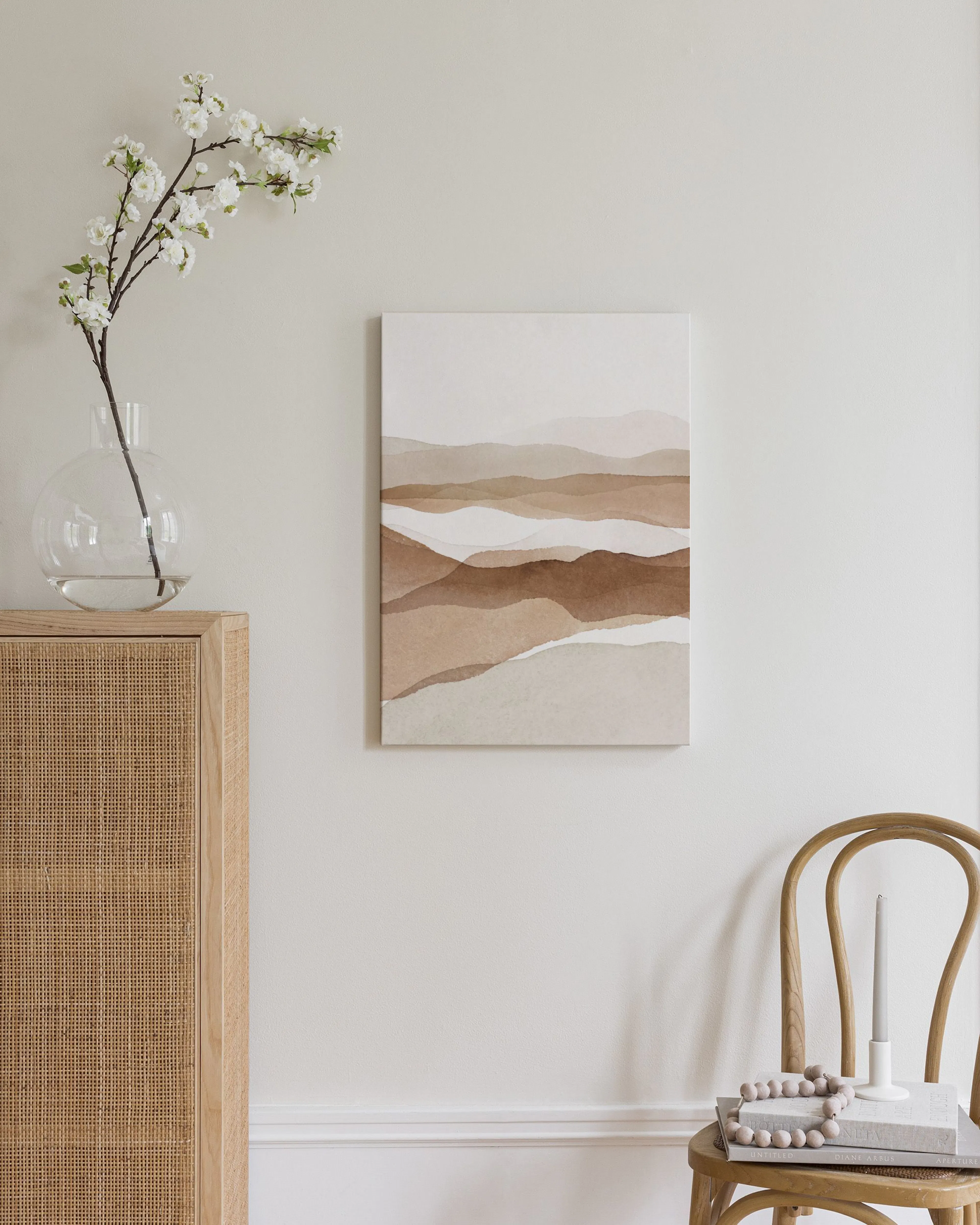 Stampa su tela di paesaggio astratto con tonalità marroni e beige, appesa sopra una credenza in legno intrecciato in una camera 