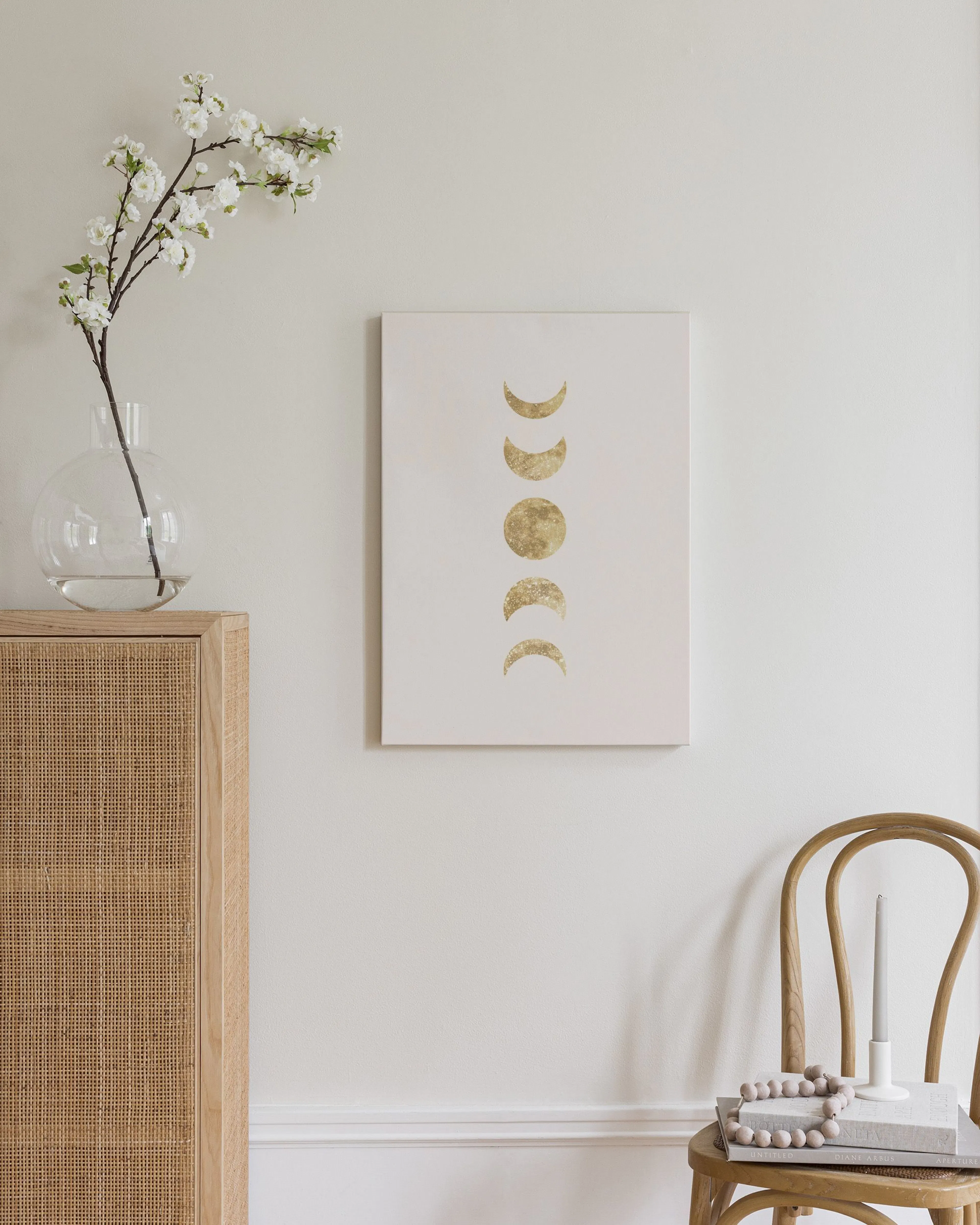 Canvas van gouden maanfasen in moderne slaapkamer, hangend boven een houten dressoir met lamp en boeken.