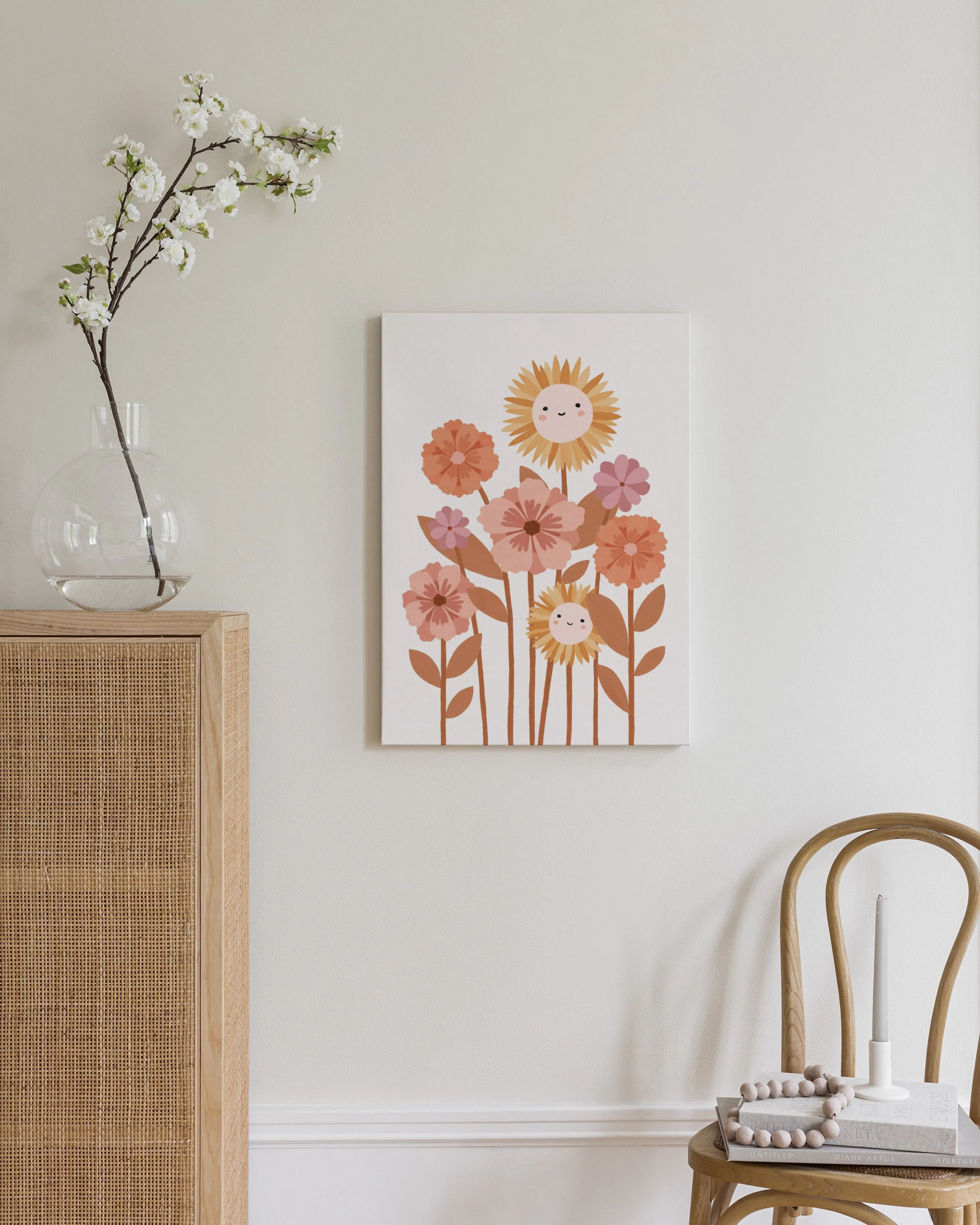 A canvas of playful cartoon flowers with smiling faces, hanging above a timber and rattan dresser in a bedroom.