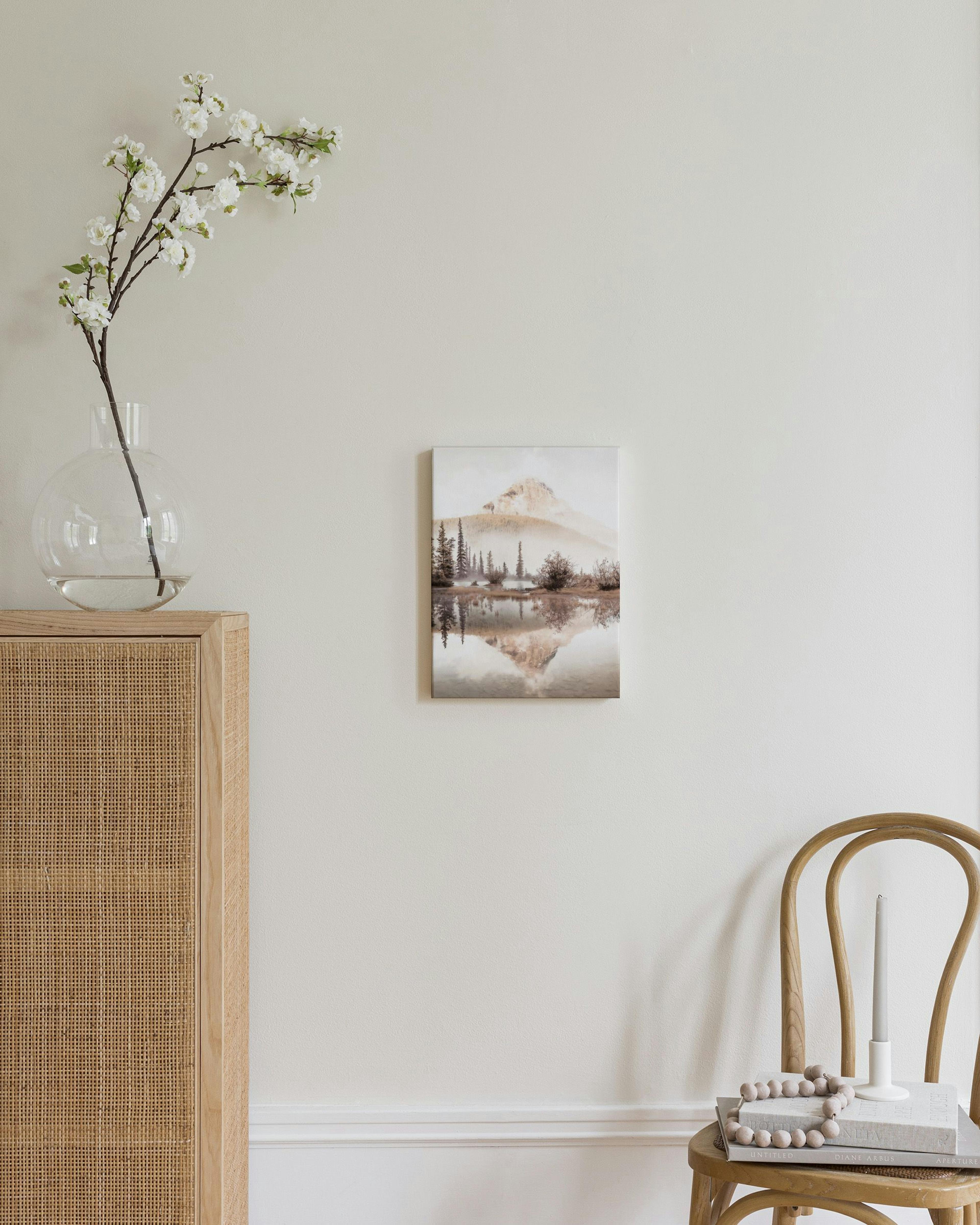 Obraz na płótnie z górskim krajobrazem, lustrzanym odbiciem w wodzie i drzewami, wiszący nad drewnianą komodą.