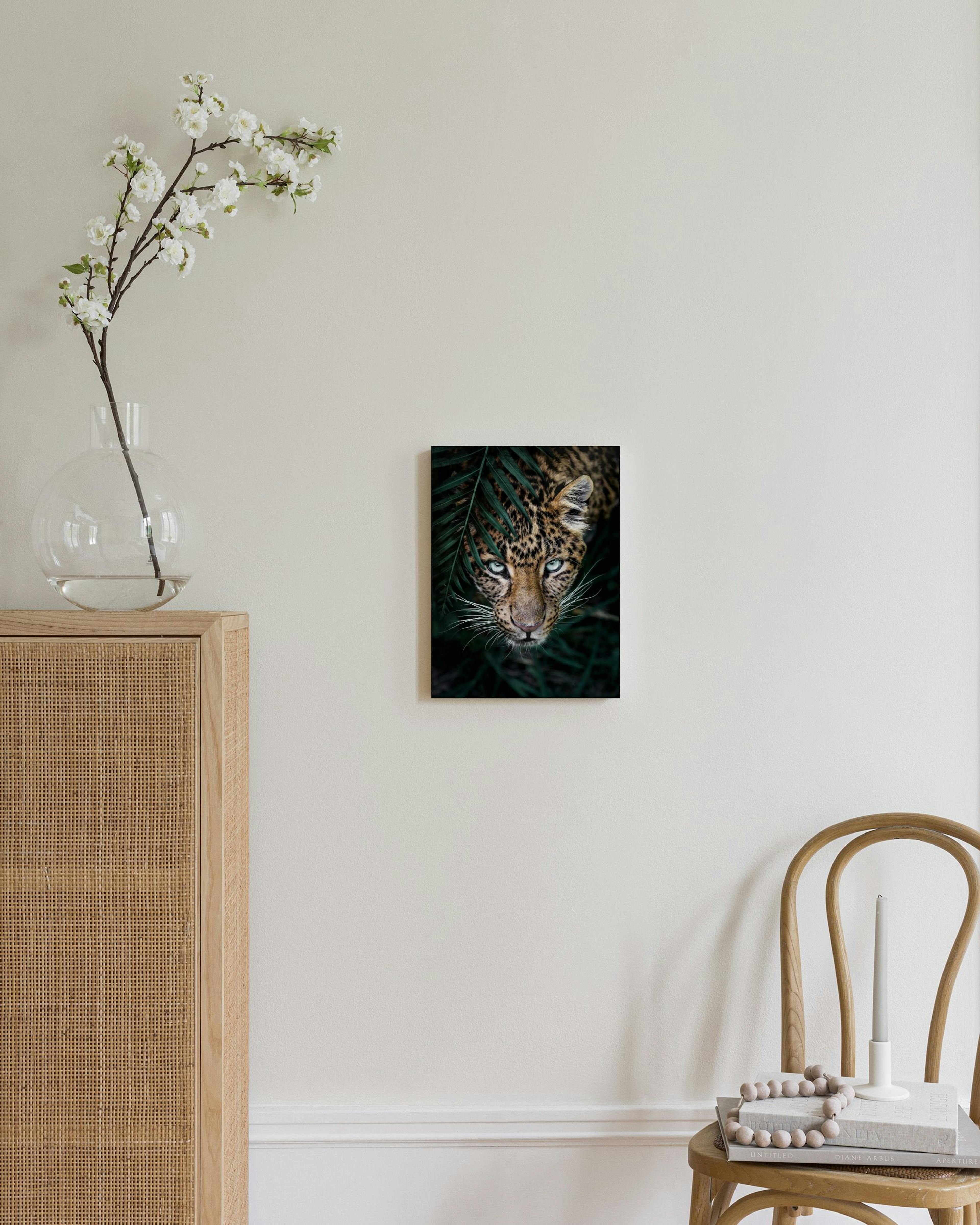 Stampa su tela di un leopardo con occhi azzurri in mezzo a foglie verdi, appesa sopra una credenza in camera da letto.