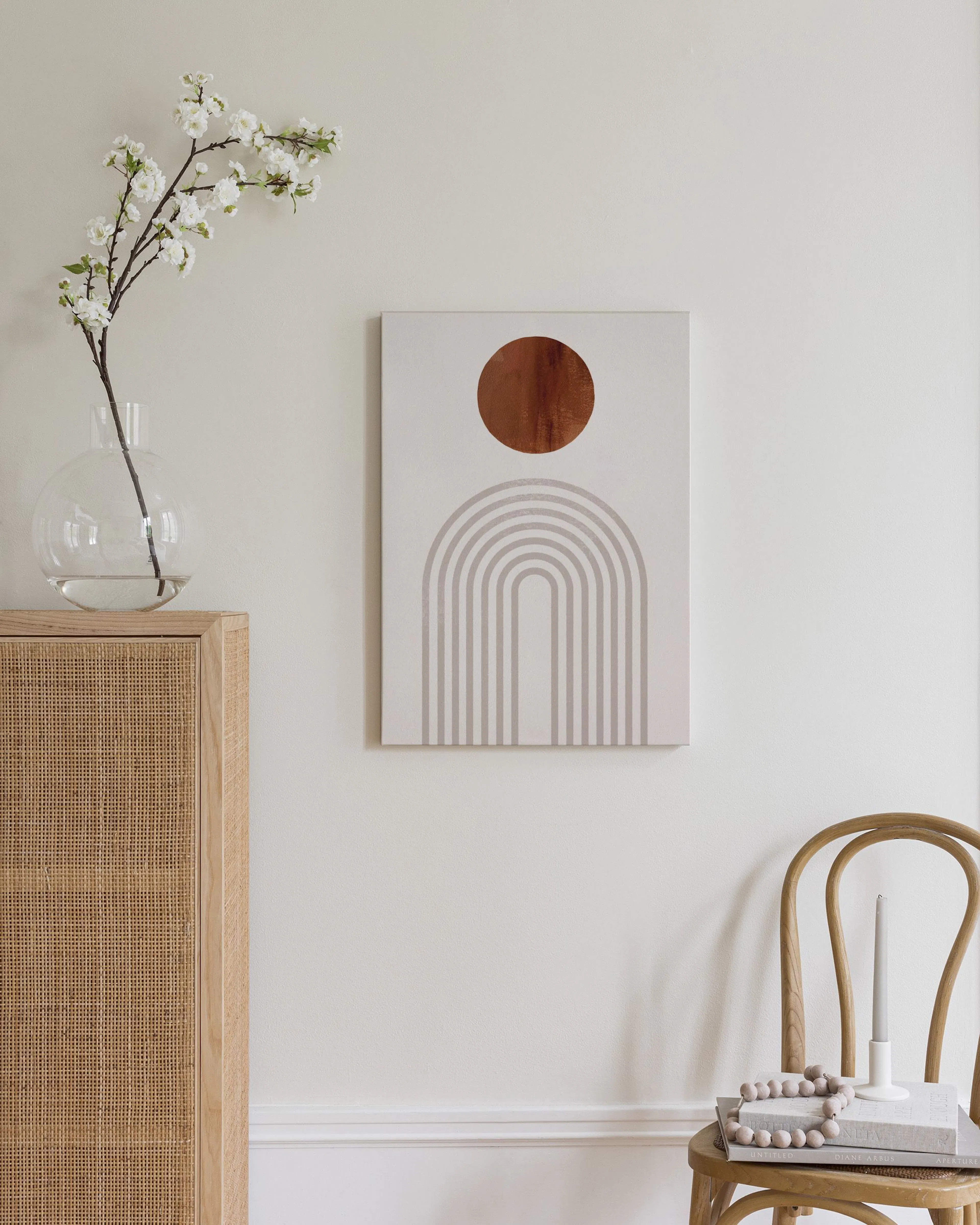 Stampa su tela con cerchio ruggine e archi grigi, appesa sopra una credenza in rattan in una camera da letto.