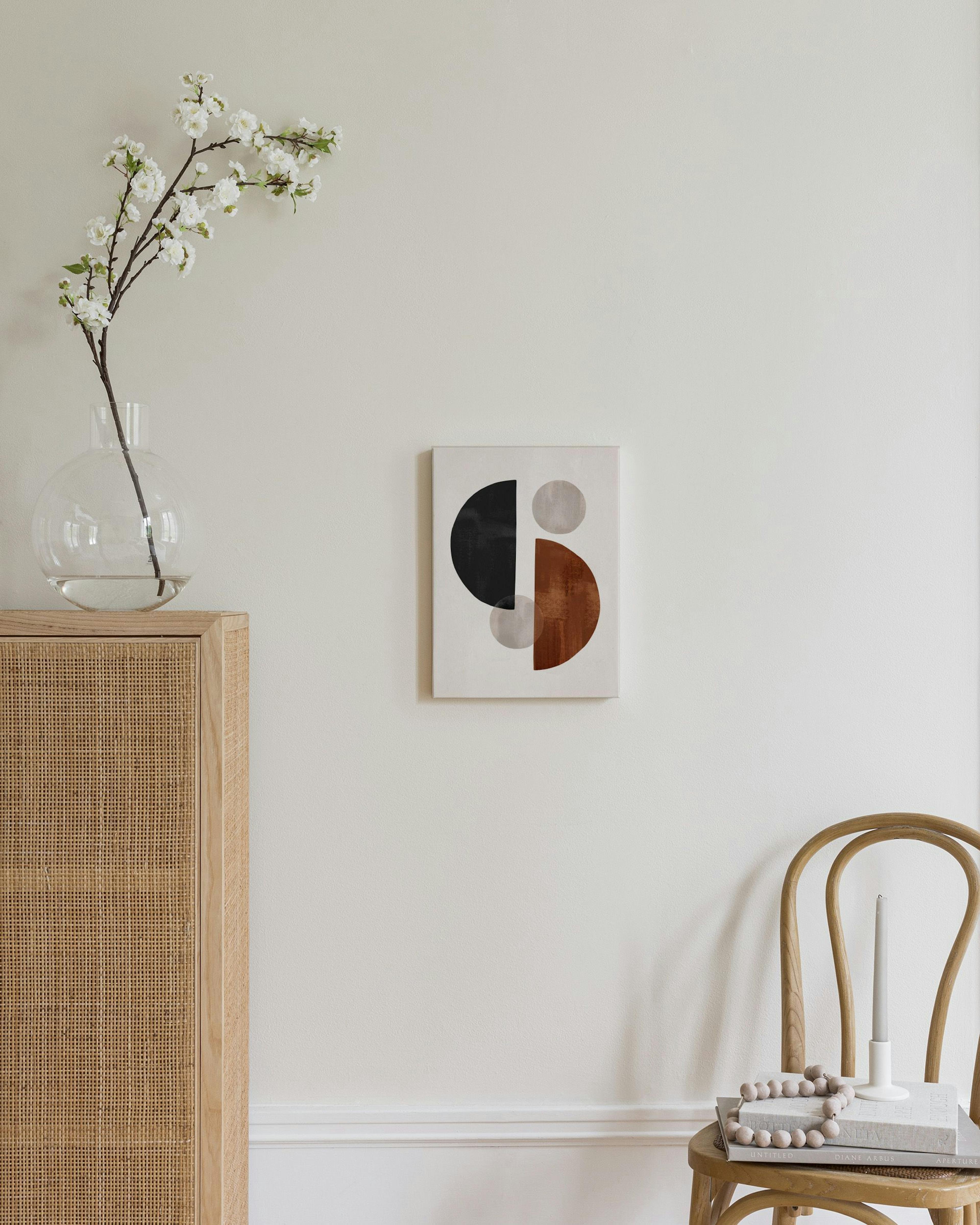 A canvas with black, rust, and gray geometric shapes, featuring semicircles and circles, hanging above a wooden cabinet in a bed