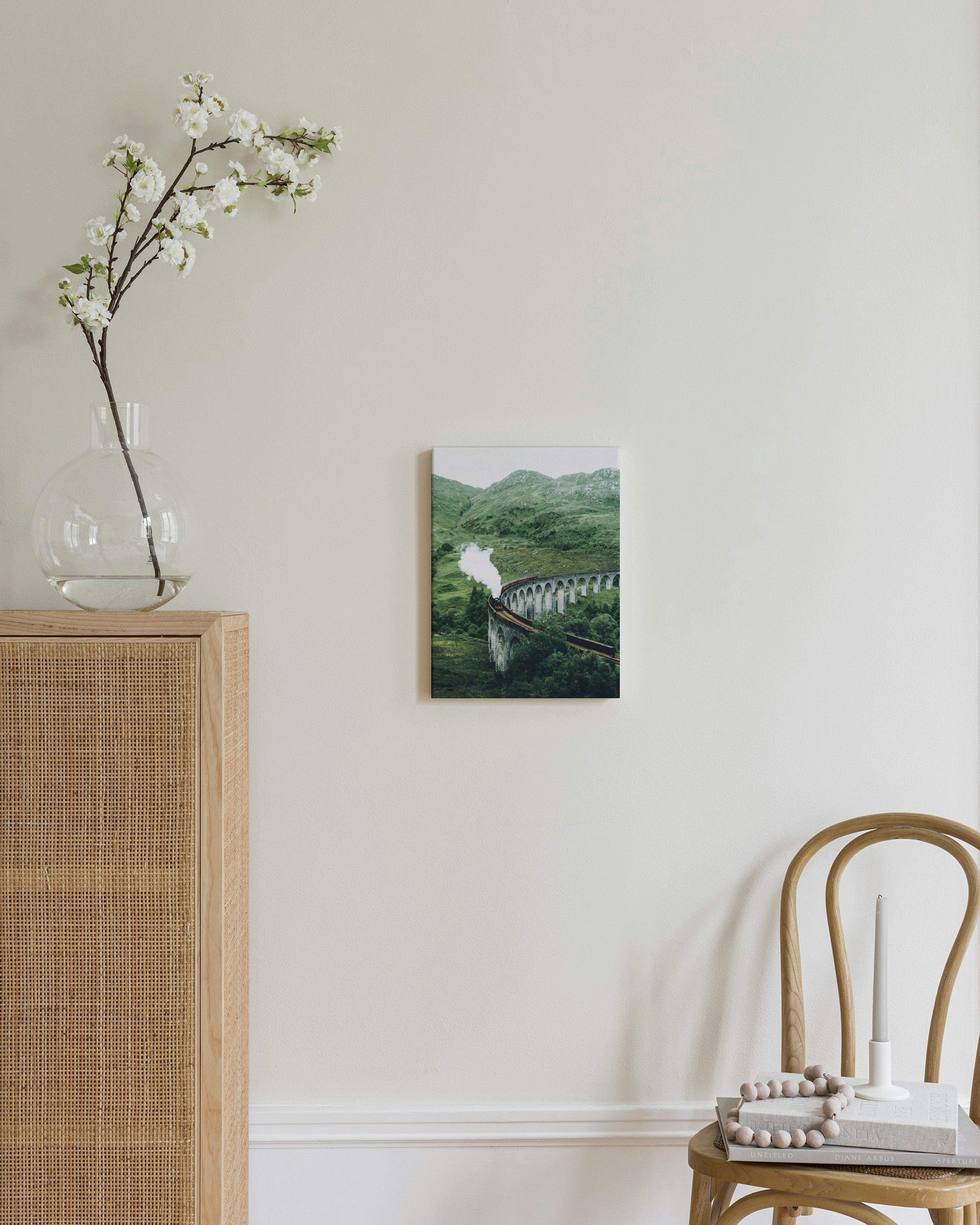 Leinwandbild mit einer Dampflok auf einem Viadukt in grüner Berglandschaft, über einem Rattankopfteil im Schlafzimmer.