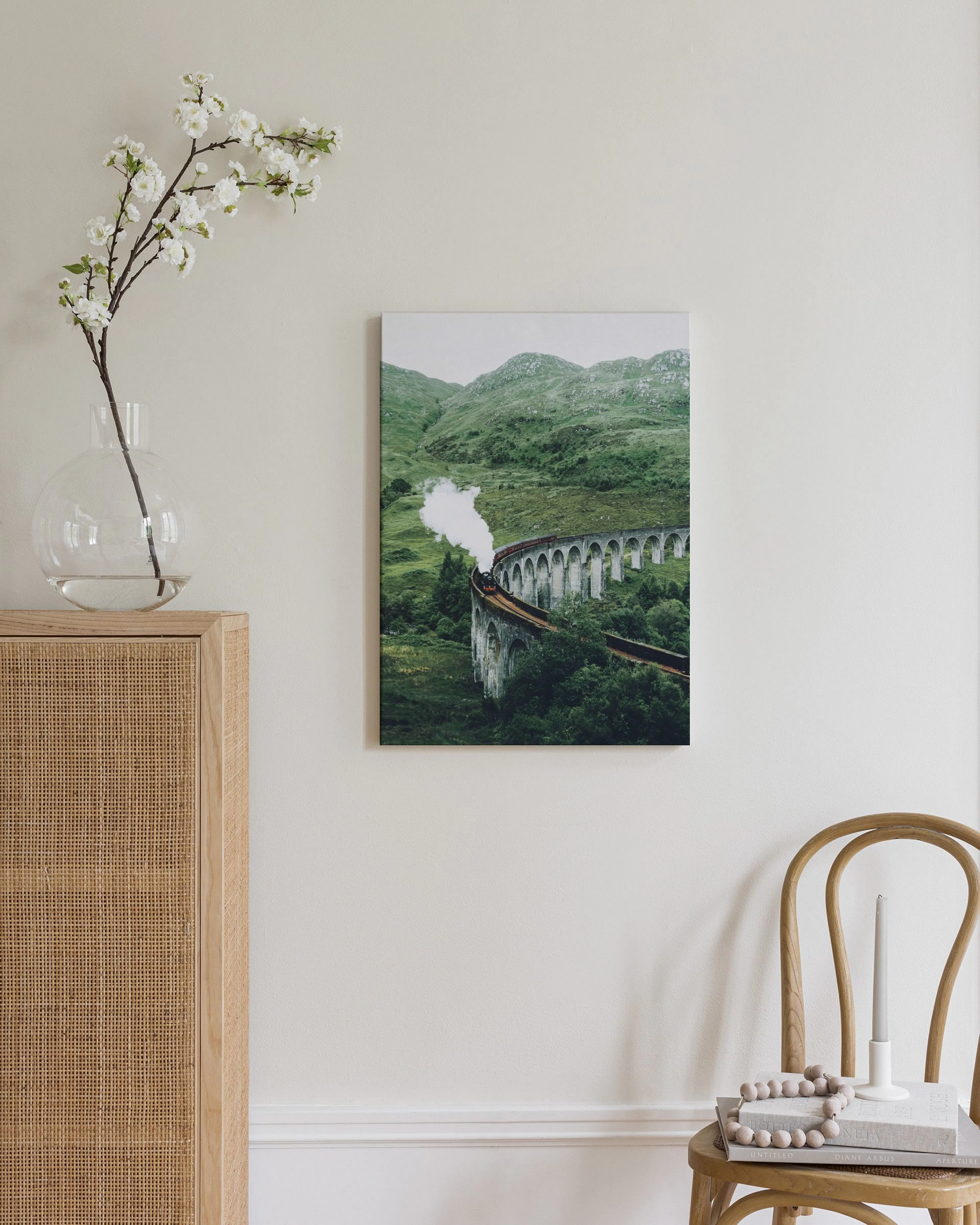 Leinwandbild mit einer Dampflok auf einem Viadukt in grüner Berglandschaft, über einem Rattankasten.