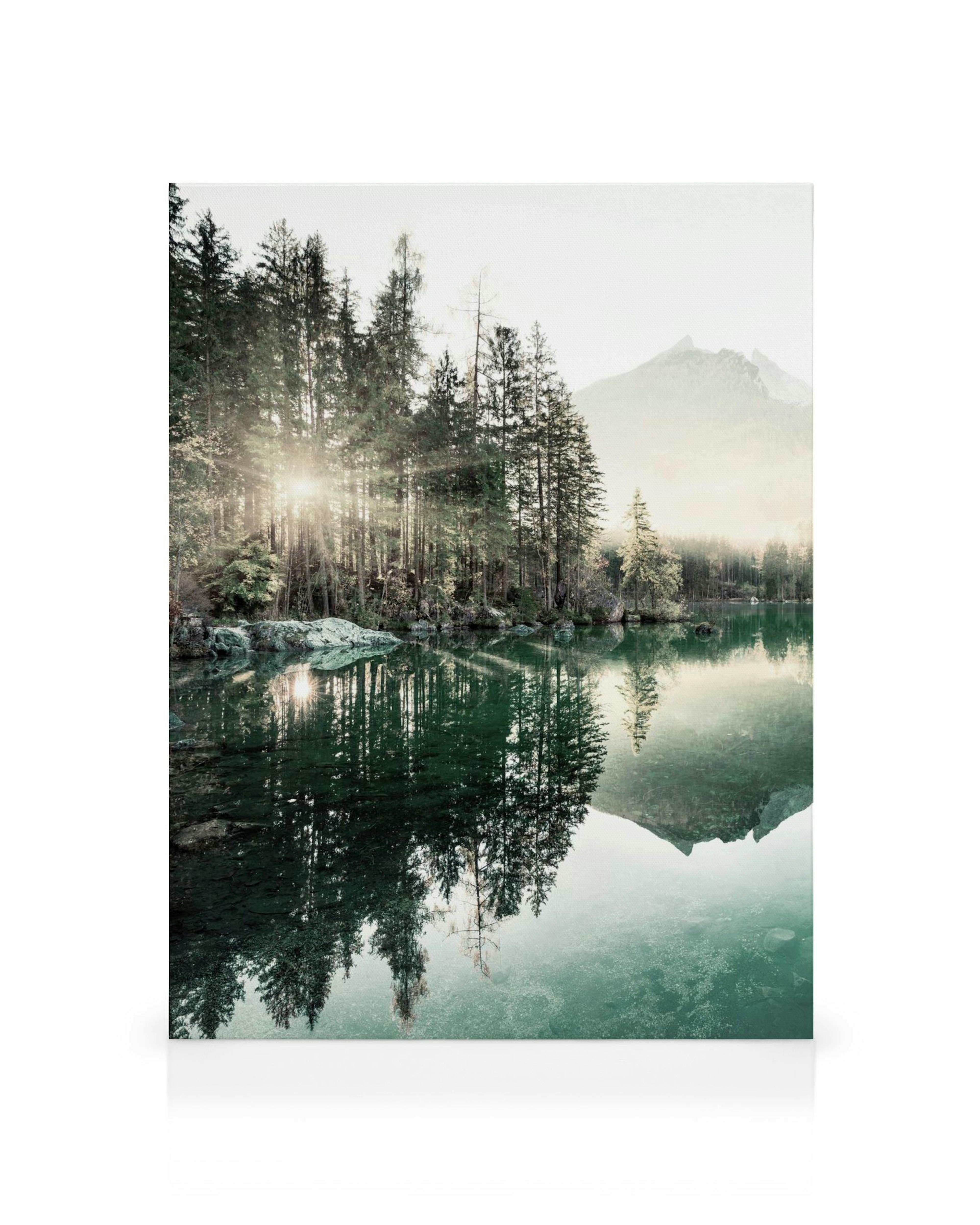 Een canvas met een mistige zonsondergang over een bergmeer met weerspiegelende bomen en bergen.