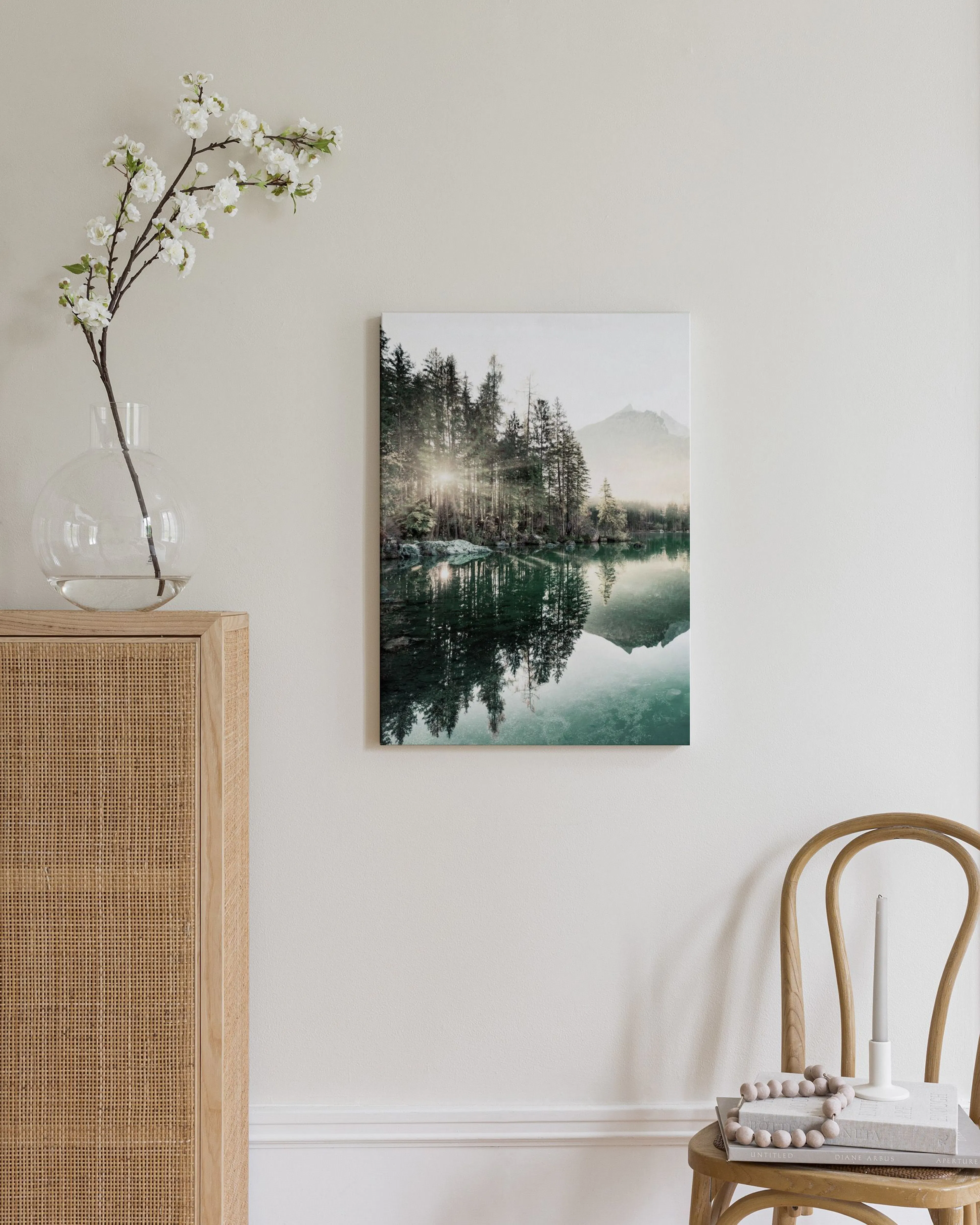 Stampa su tela di un lago di montagna con abeti e riflessi, appesa sopra una cassettiera in legno chiaro.
