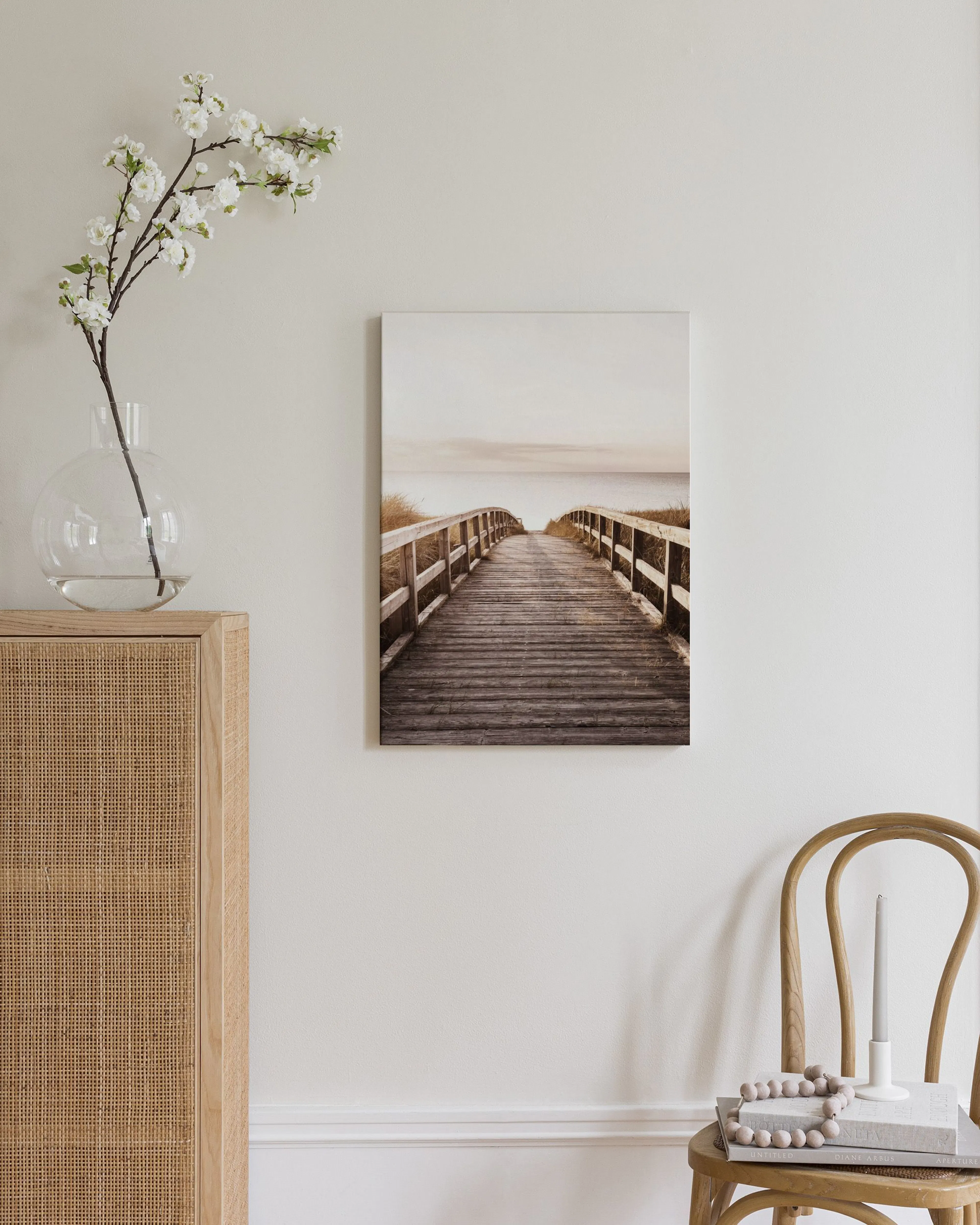 Leinwandbild eines Holzstegs zum Meer bei Sonnenuntergang, über einem Rattan-Sideboard im Schlafzimmer.
