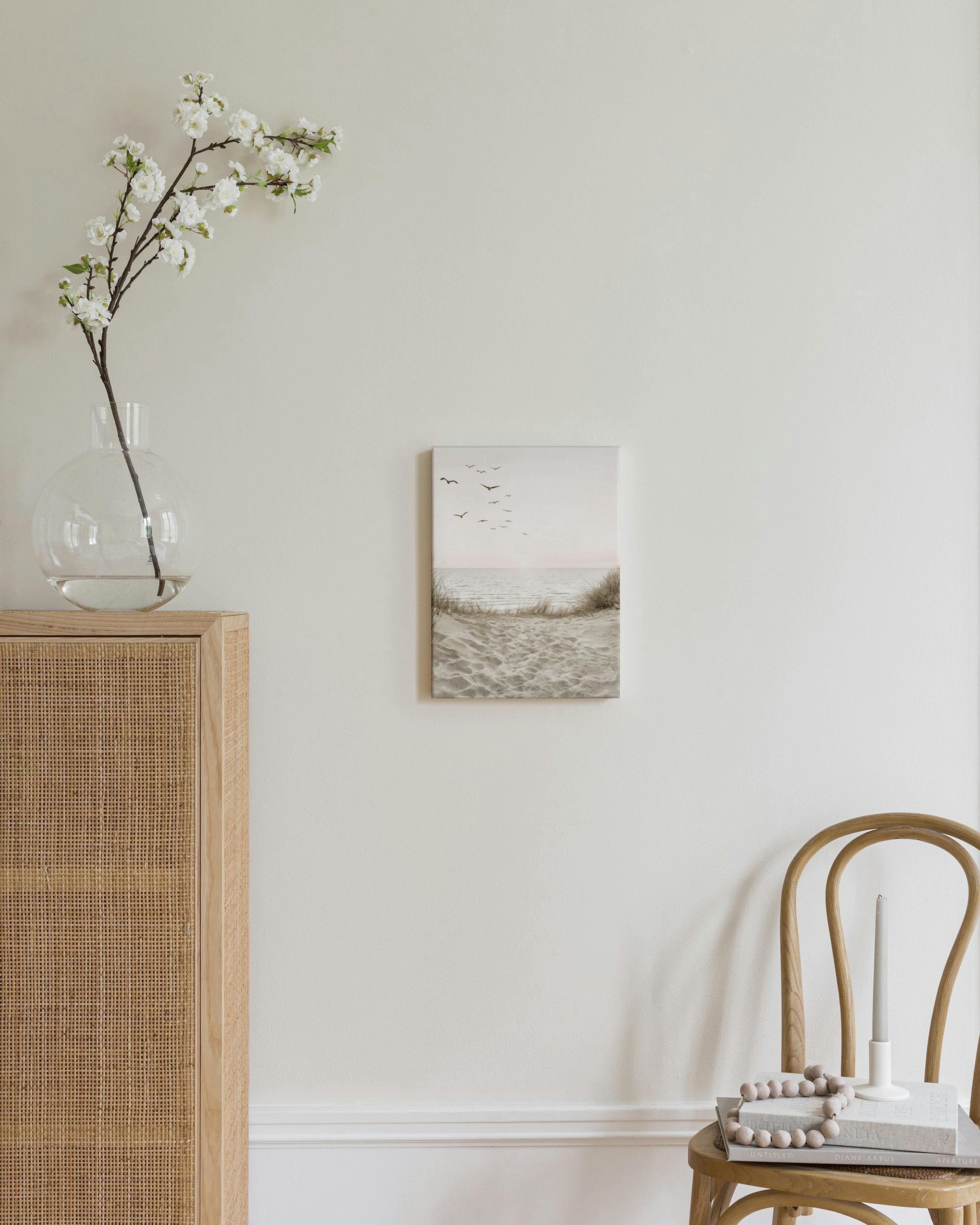 Toile dune plage au coucher du soleil avec des oiseaux en vol, accrochée au-dessus dune commode en rotin.