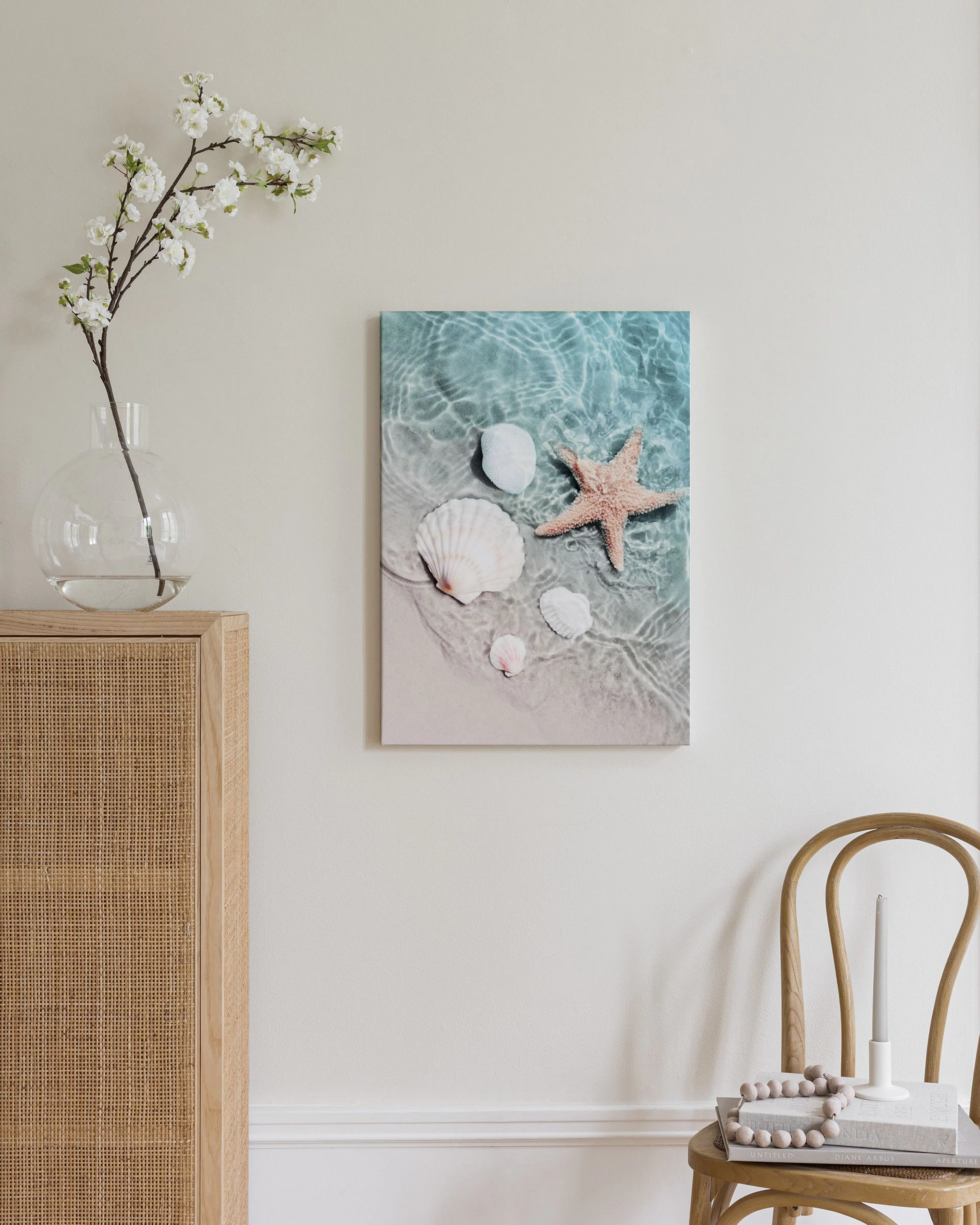 A coastal canvas of seashells and a starfish on a sandy beach submerged in water, displayed above a wooden dresser.