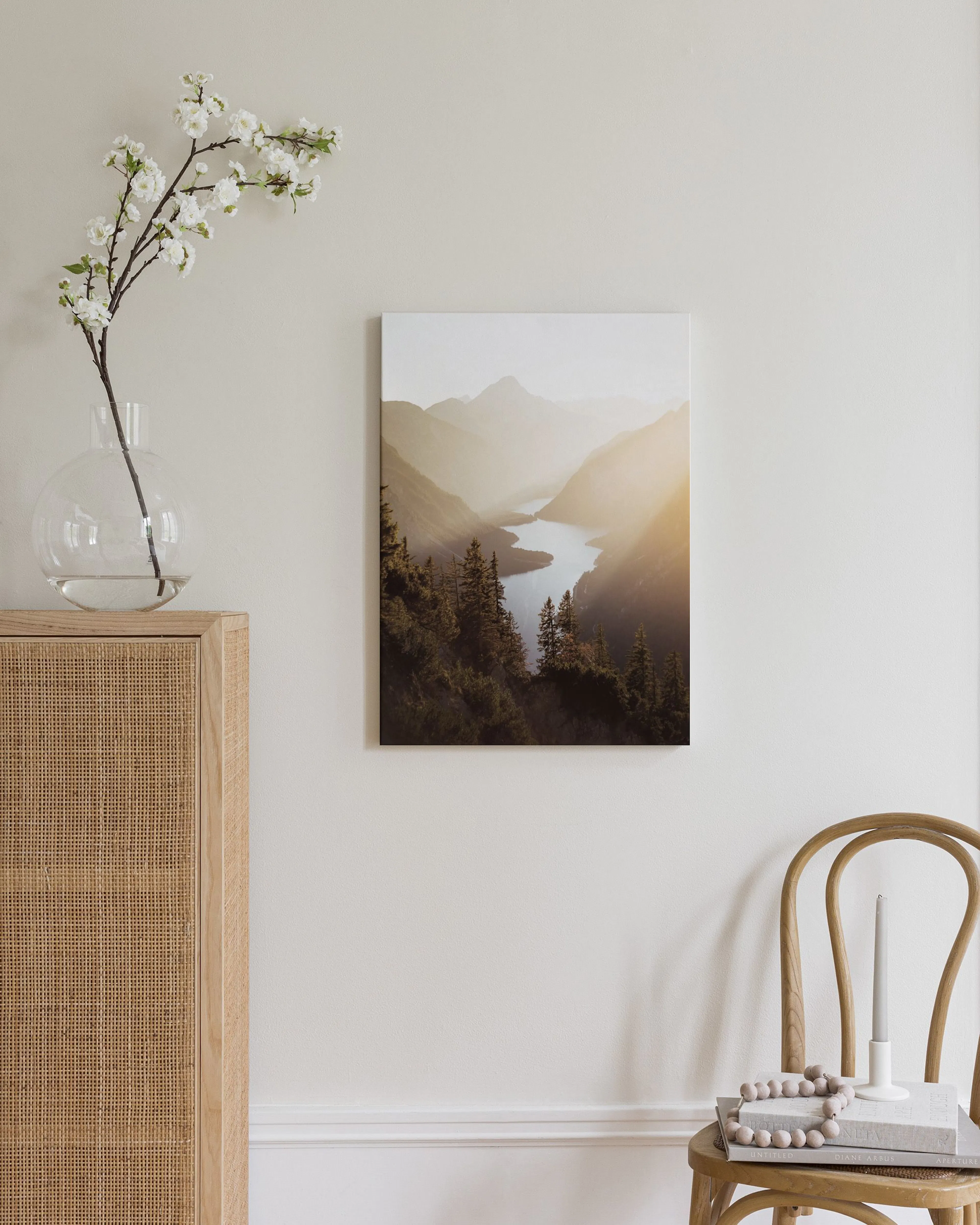Toile murale paysage montagneux brumeux avec lac et forêt, suspendue au-dessus dun meuble en rotin clair dans une chambre.