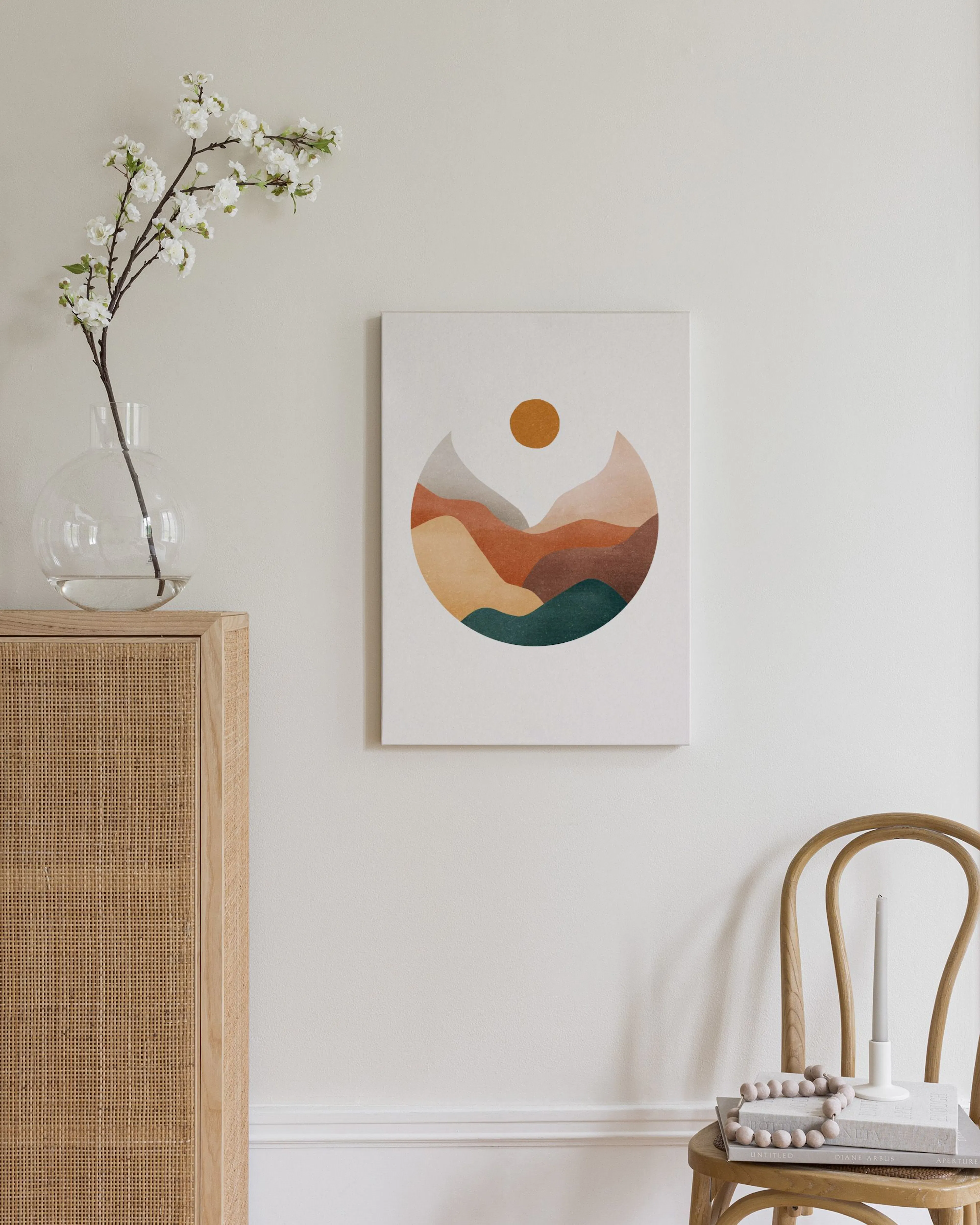 Toile murale abstraite de montagnes colorées et soleil, accrochée au-dessus dune commode en bois et rotin.