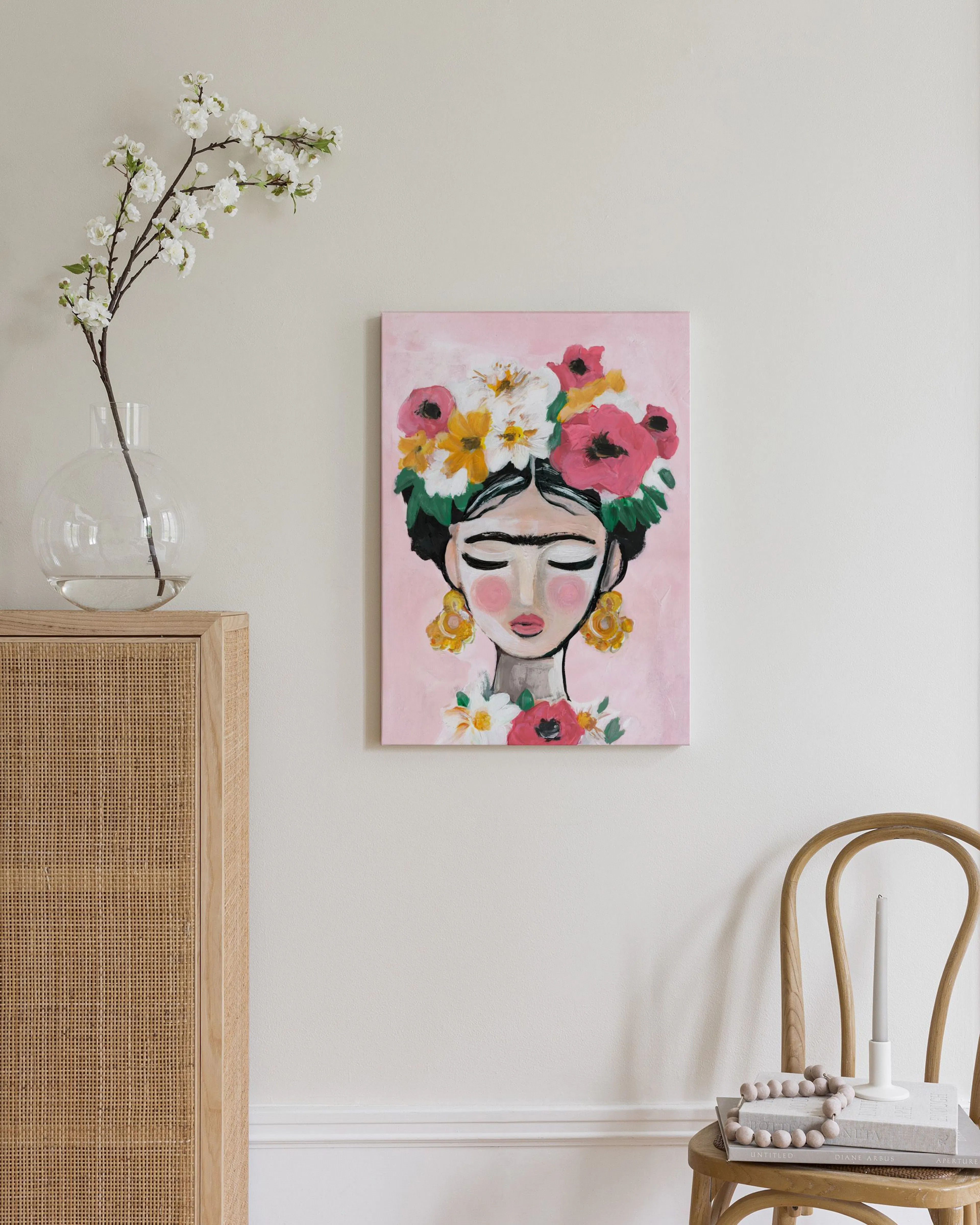 Toile murale portrait de femme aux fleurs roses et jaunes sur fond rose pâle, au-dessus dune commode en rotin.