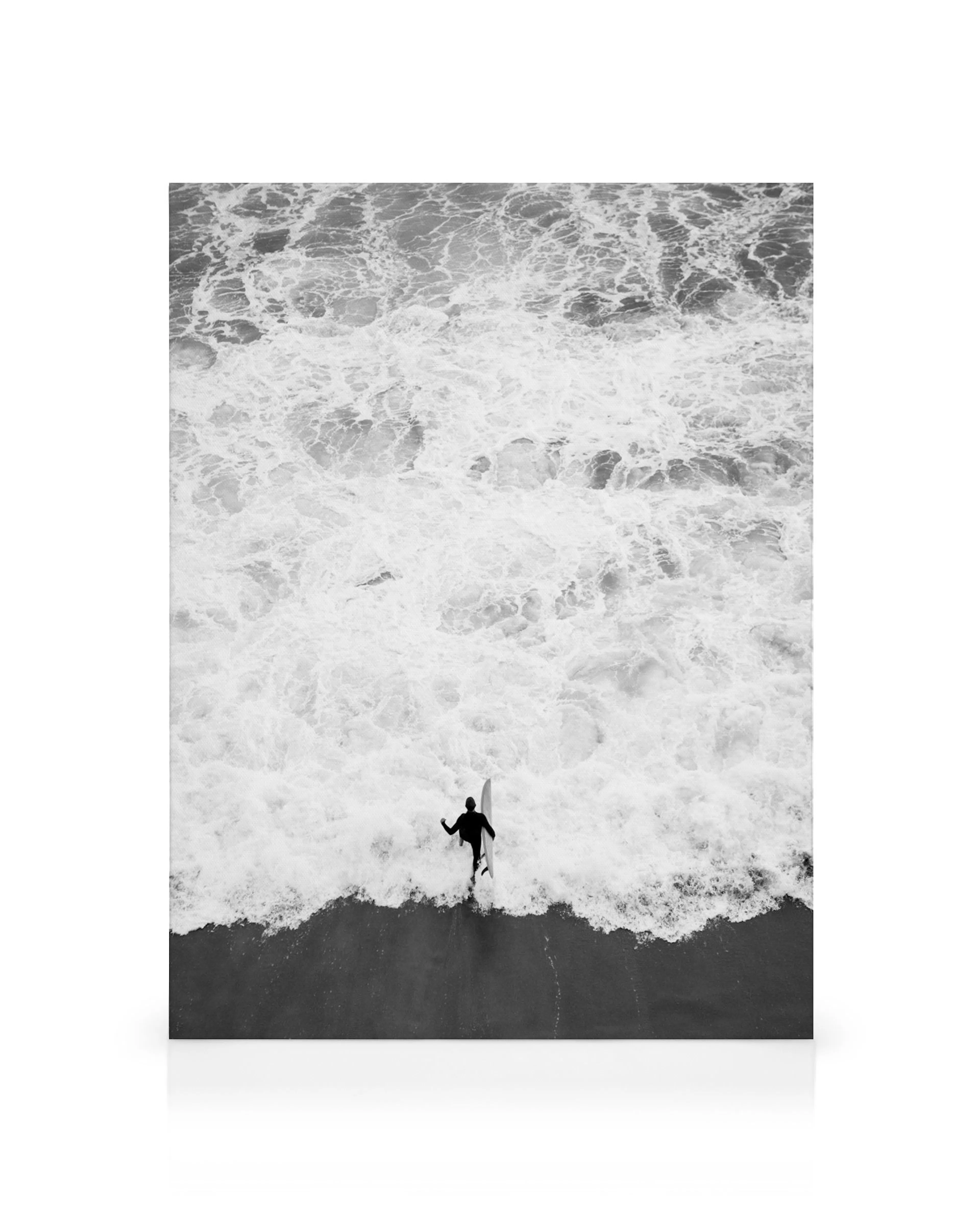 A black and white canvas of a surfer in a wetsuit walking into the ocean with a surfboard, waves crashing around.