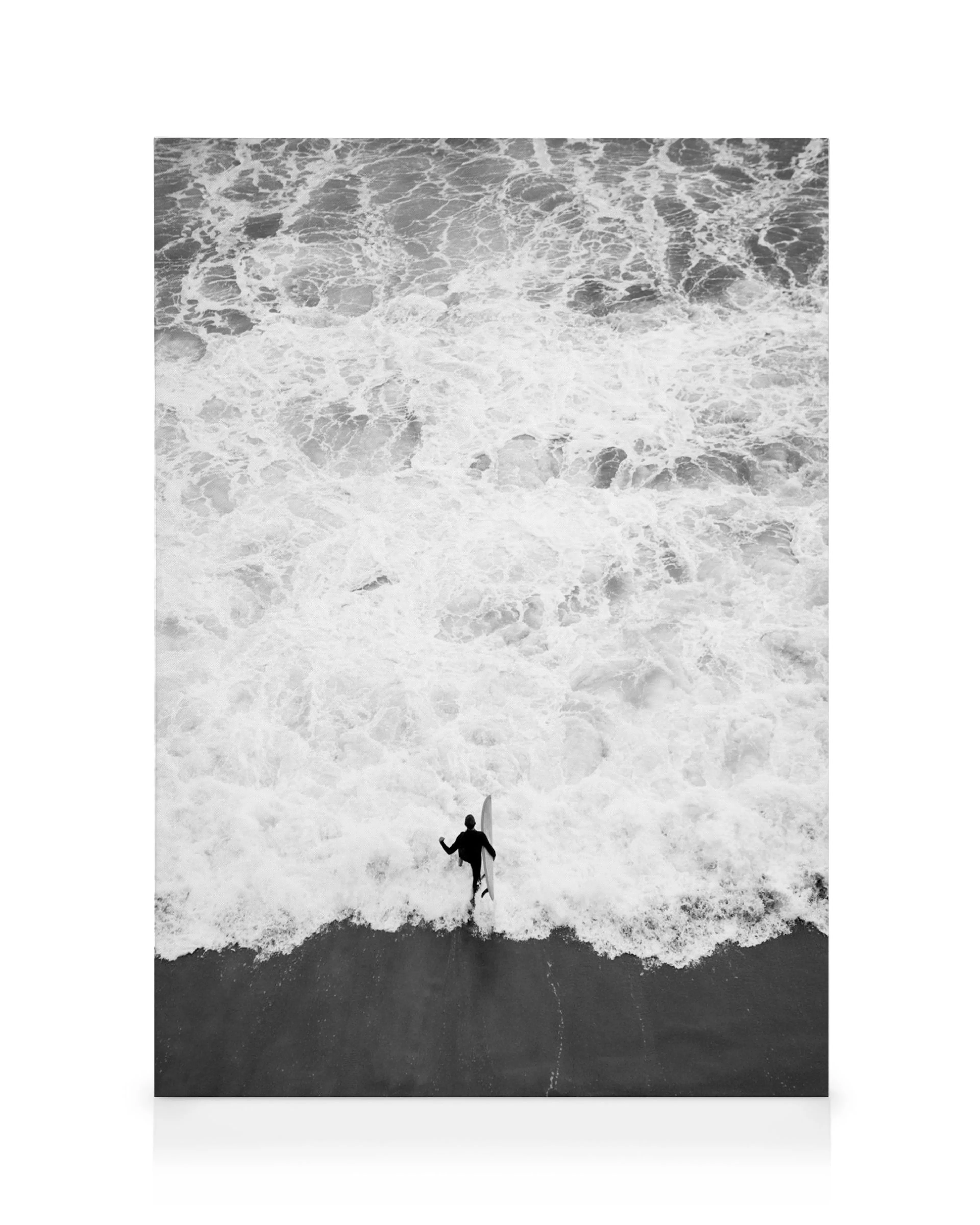 A black and white canvas of a lone surfer walking into the frothy ocean, holding a surfboard.