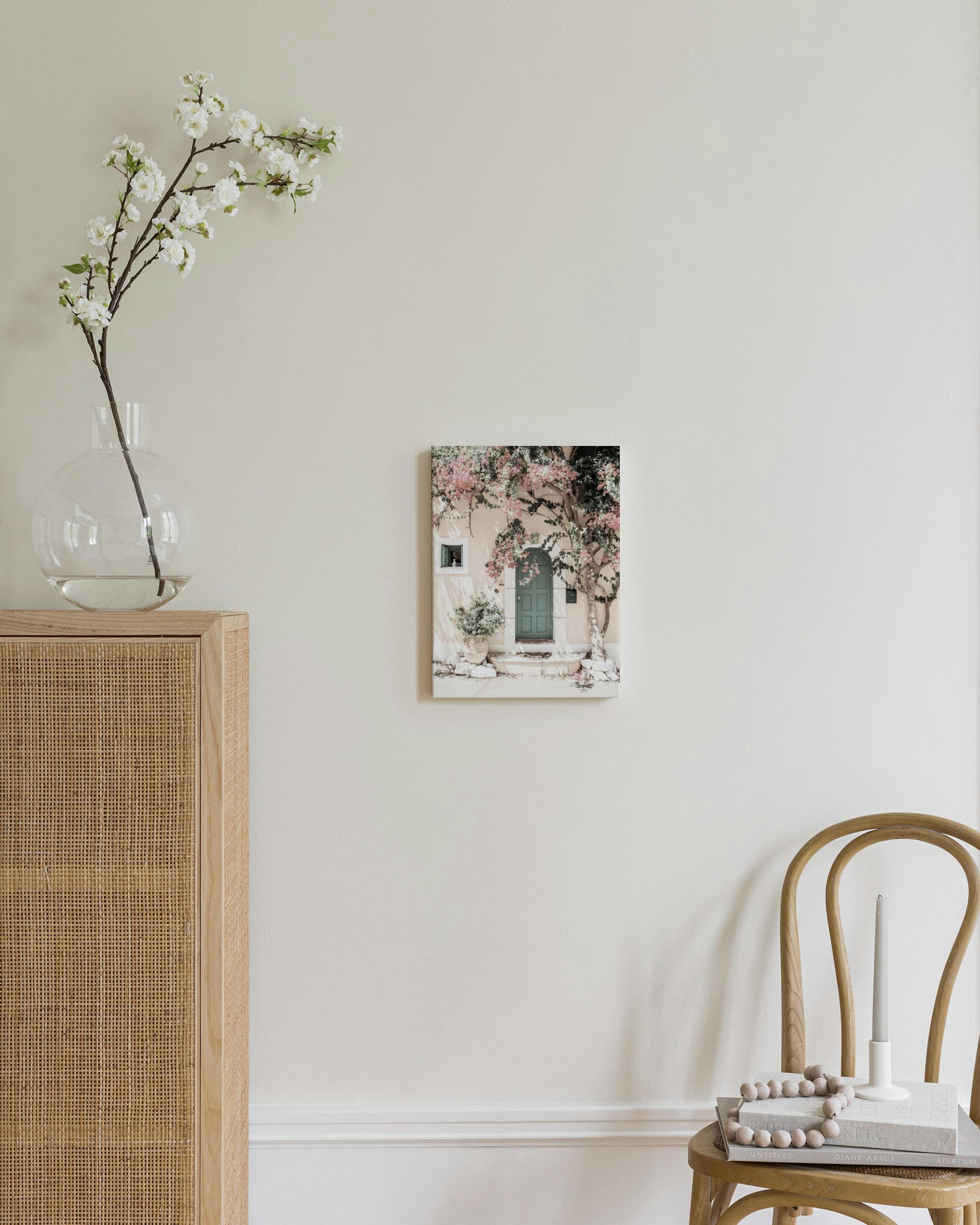 Obraz na plátně s růžovými květy a zelenými dveřmi na světlé fasádě, visící v moderním obývacím pokoji.