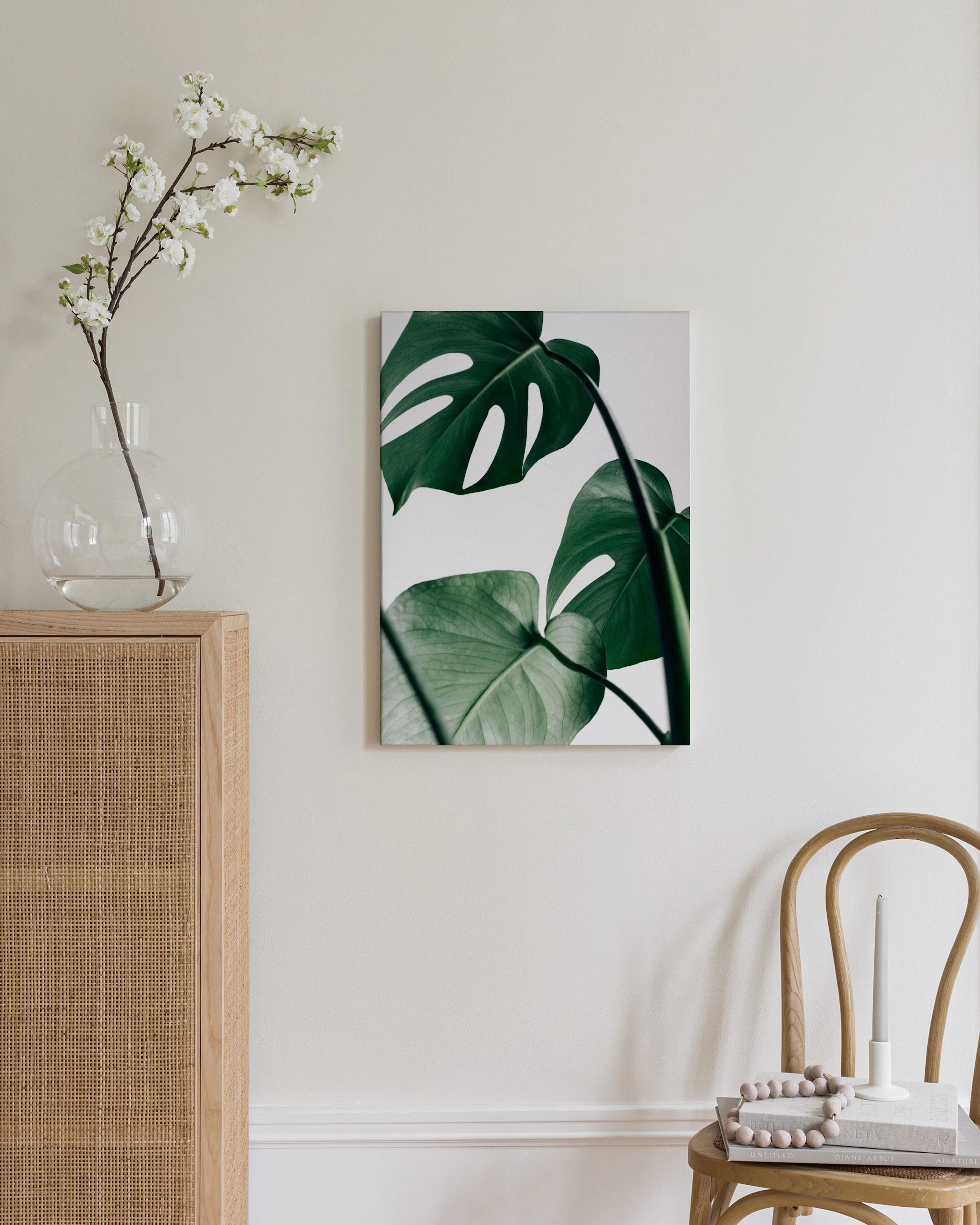 Stampa su tela con foglie di Monstera verdi, appesa in un ambiente moderno con vaso e pouf.