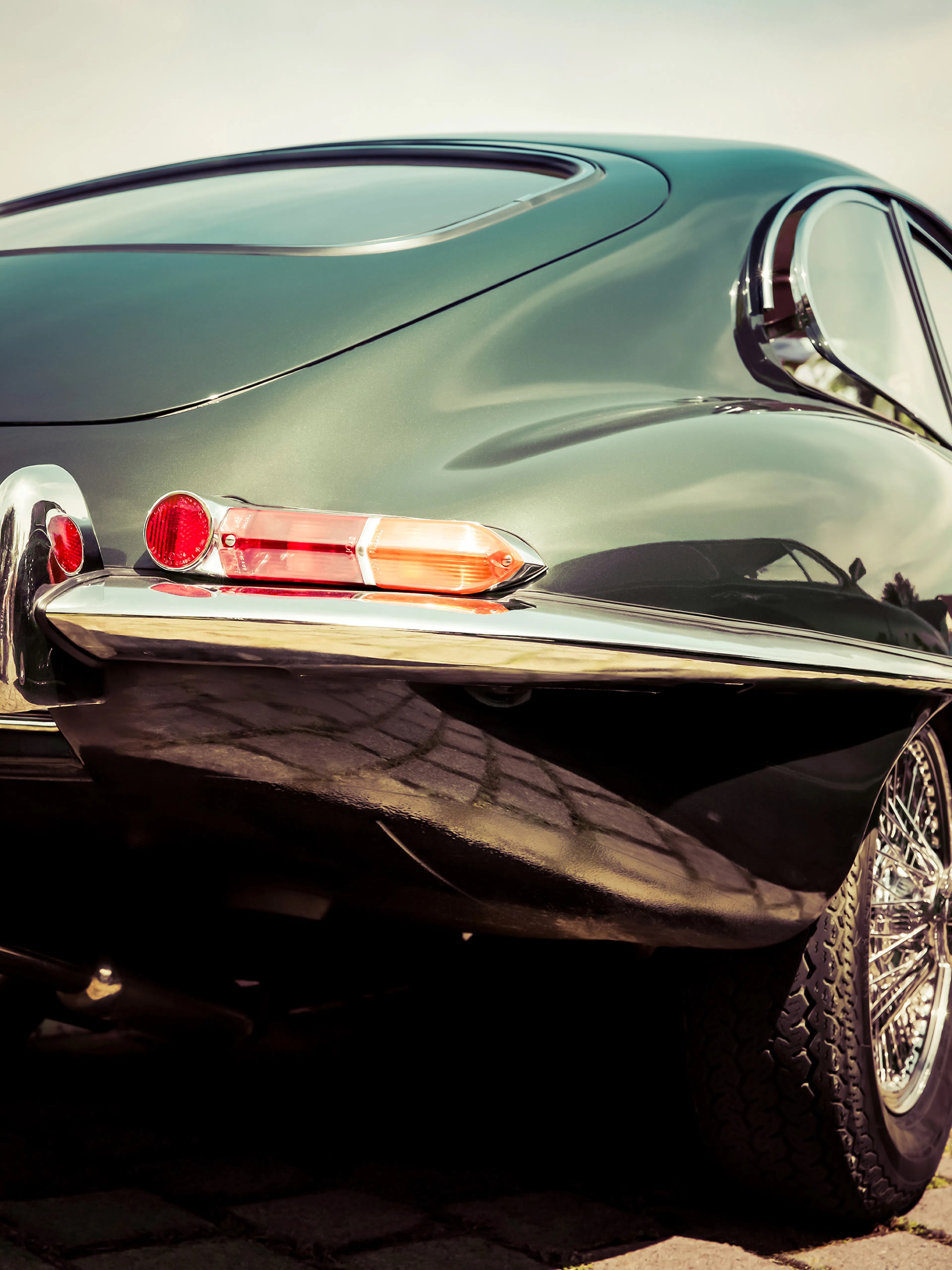 A poster featuring the rear view of a dark green vintage sports car with red taillights and chrome trim.